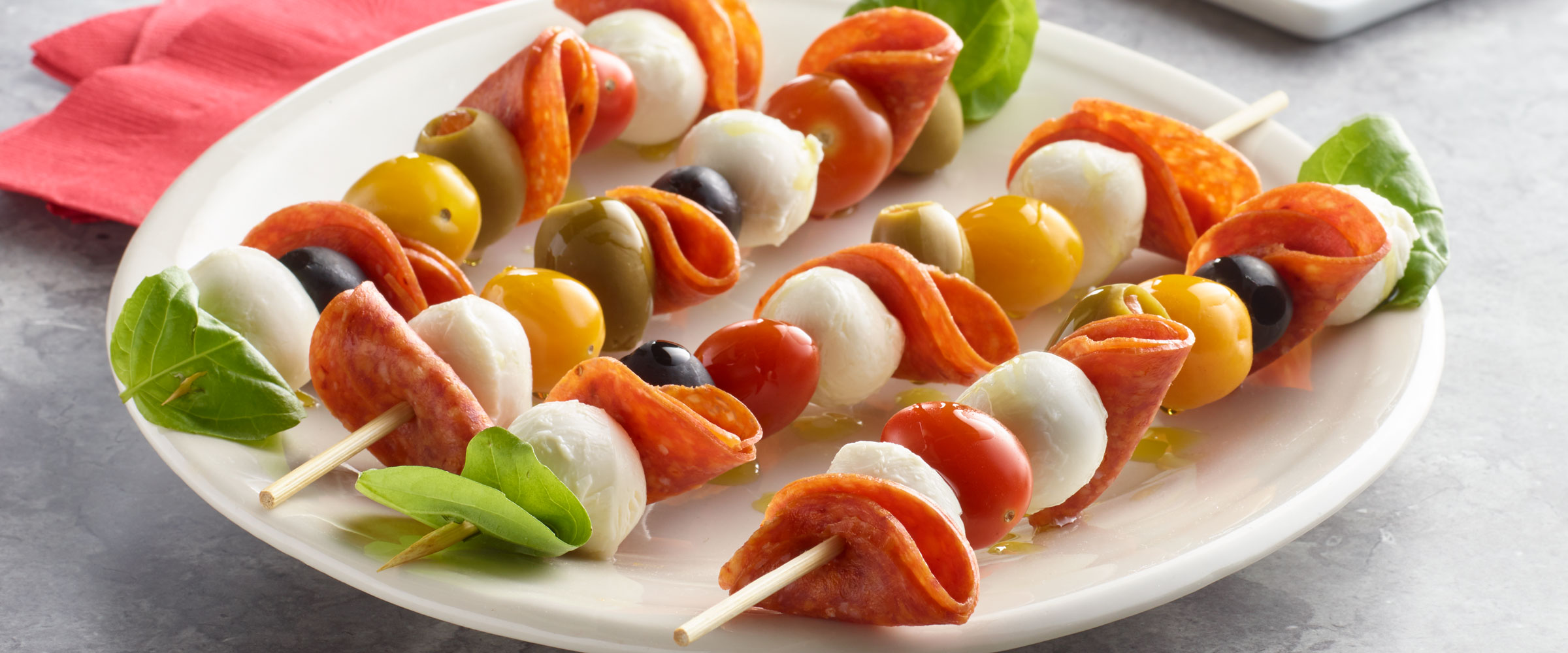 Pepperoni Antipasto Skewers with olives, tomatoes and mozzarella on white plate