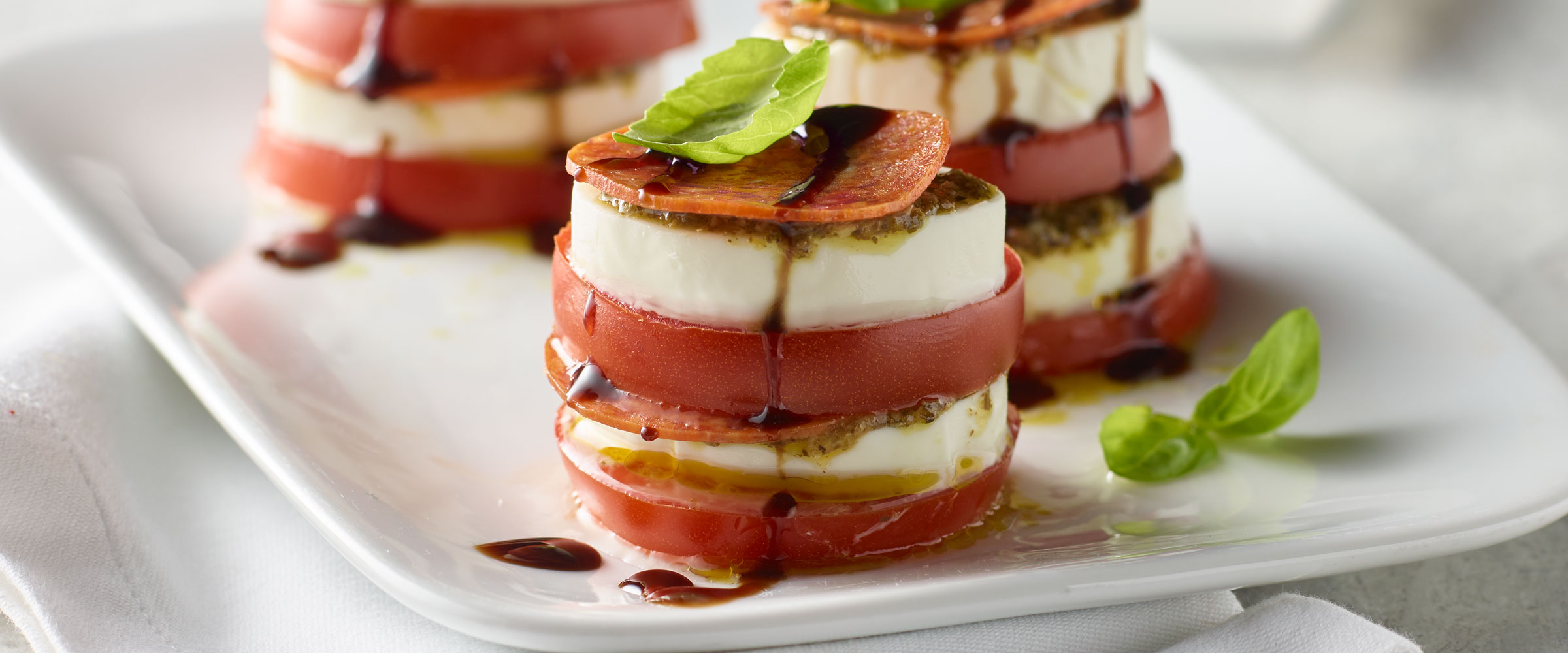 Pepperoni Caprese tower on white plate drizzled with balsamic