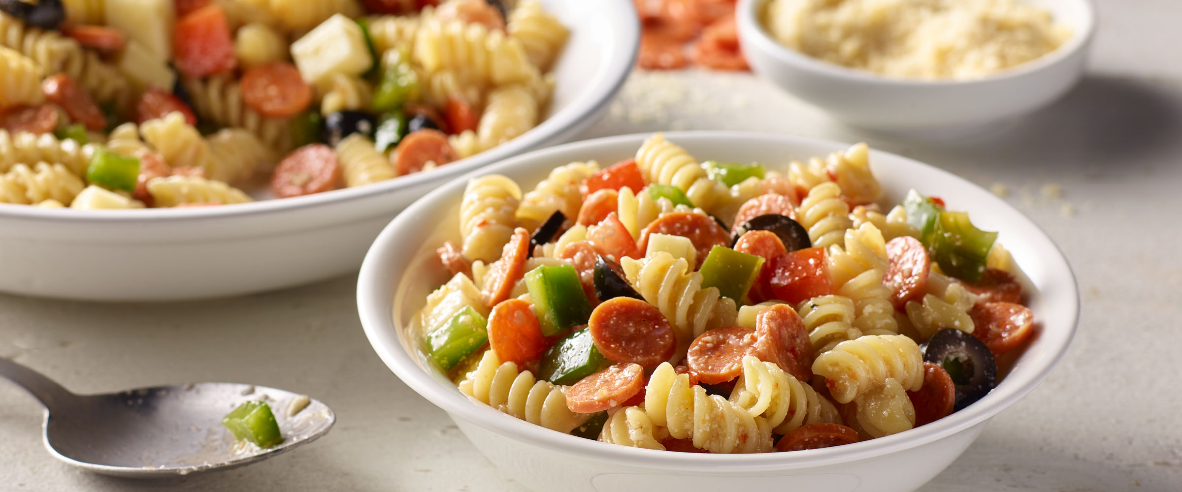 Pepperoni Minis Pasta Salad in white bowl with serving spoon