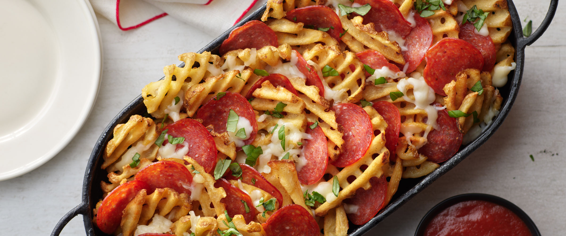 Pizza waffle fries topped with pepperoni in black dish