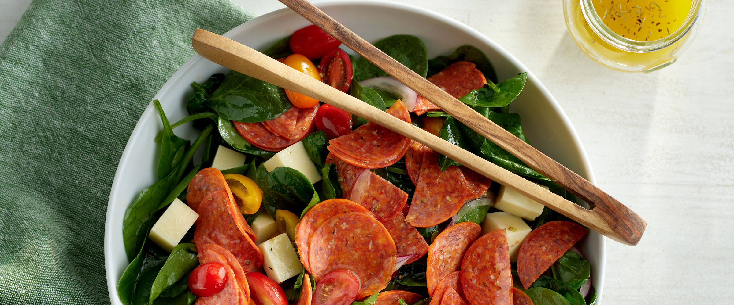 Pepperoni Spinach Salad with Mozzarella and Tomatoes on green napkin with serving tongs