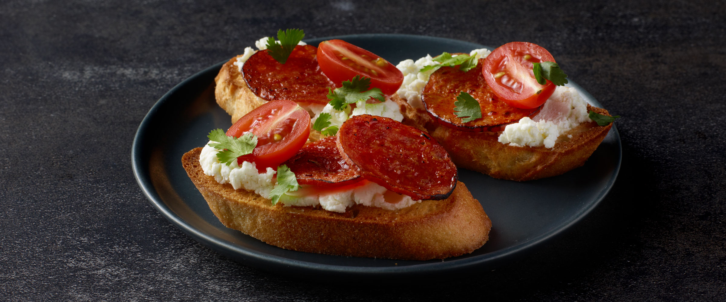 Chorizo Toasts with Goat Cheese and Tomato on plate topped with garnish