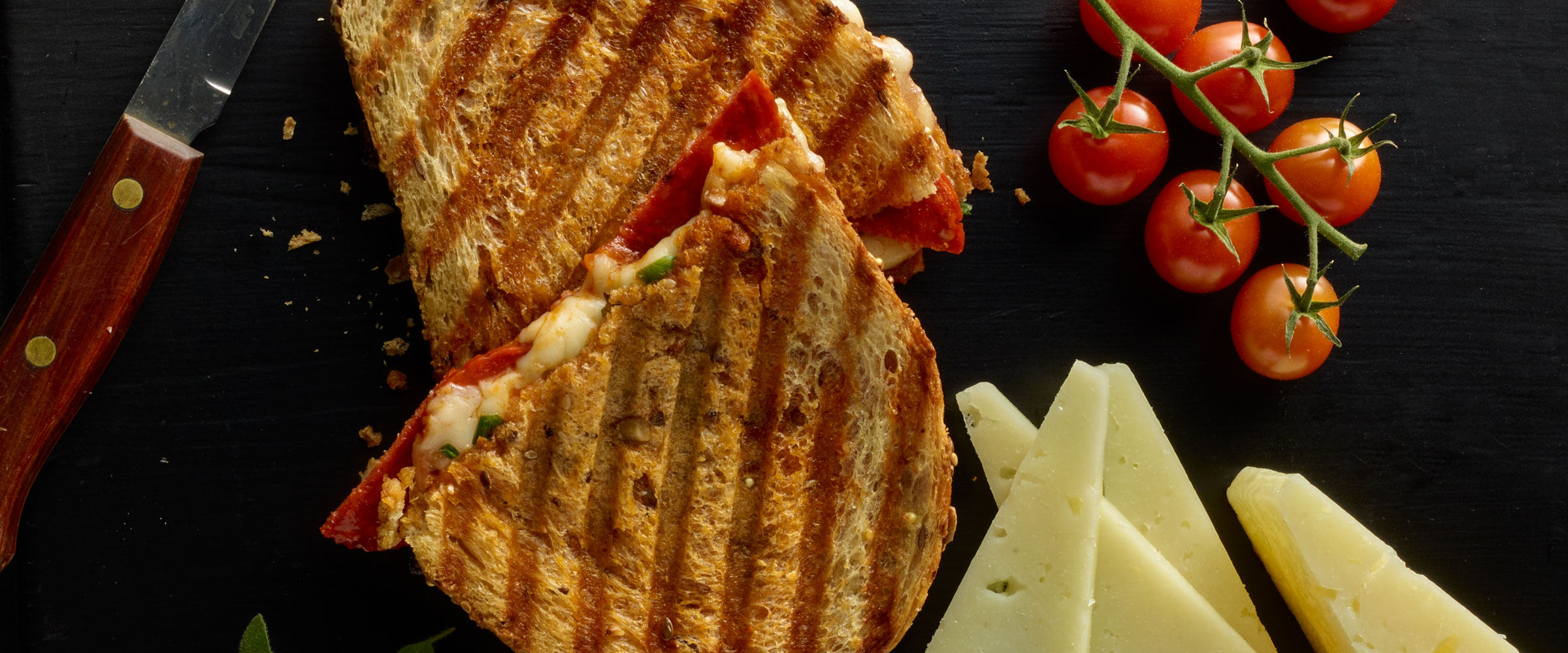 Chorizo Panini sliced in half with cheese and tomatoes on side