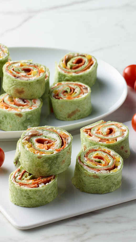 spinach wraps with pepperoni, peppers and cream cheese on a white serving tray