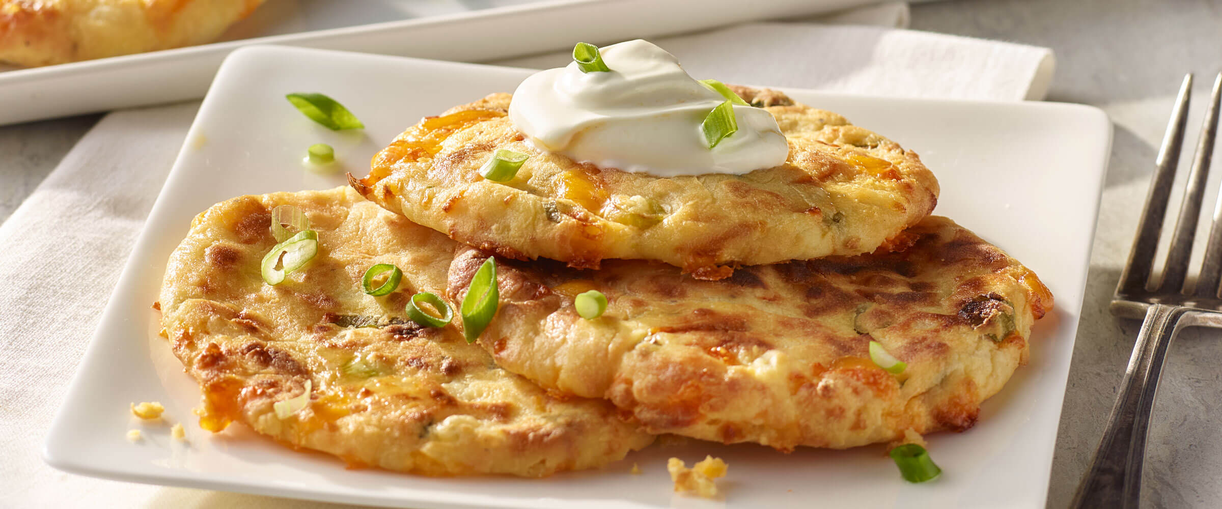 Air Fryer Mashed Potato Pancakes topped with sour cream and green onions on white plate