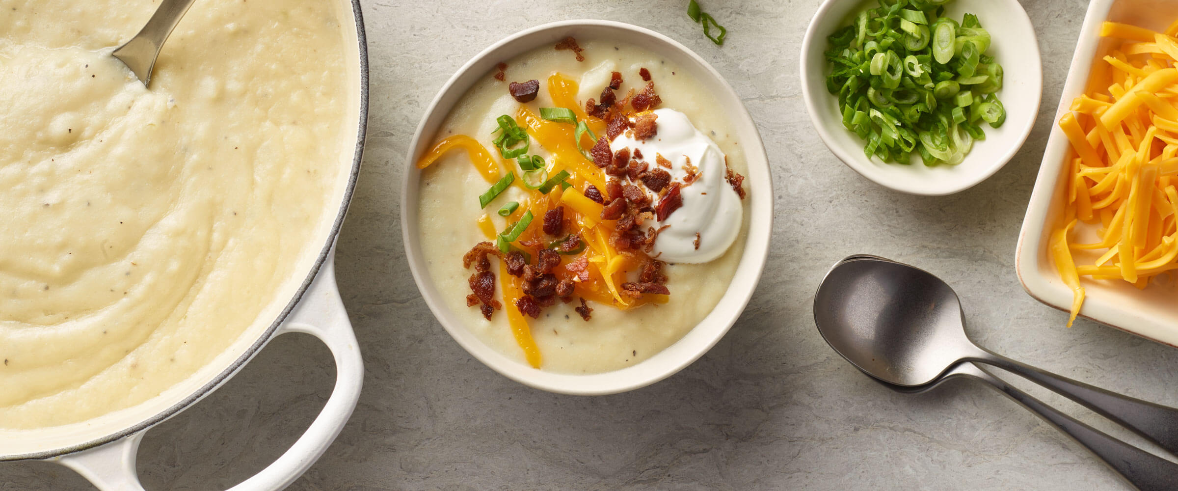 Loaded Mashed Potato Soup topped with bacon, cheese, sour cream and green onions in white bowl