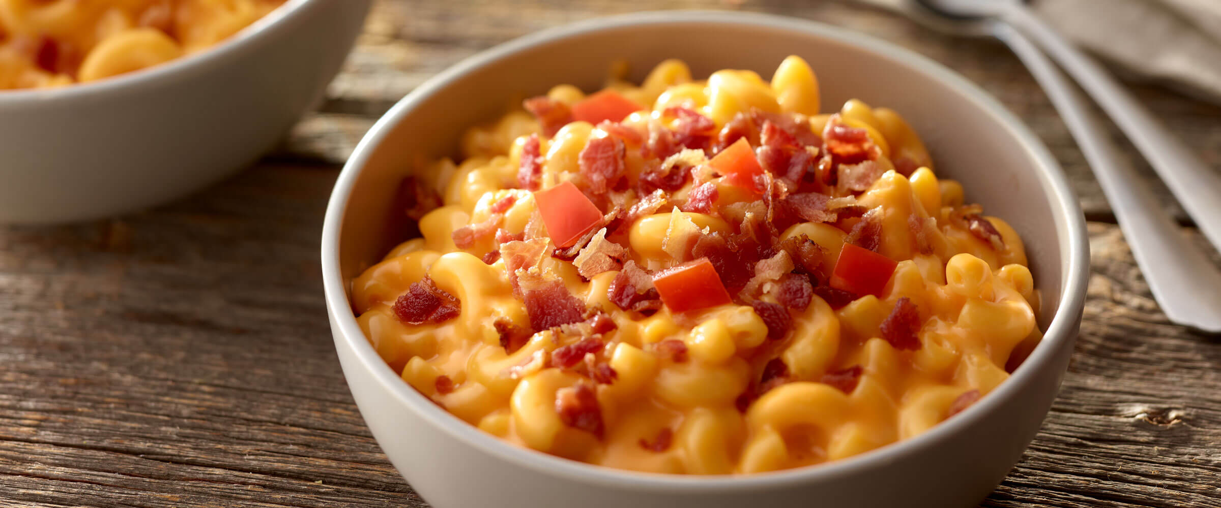 Triple Macaroni & Cheese topped with bacon bits and tomatoes on wood table