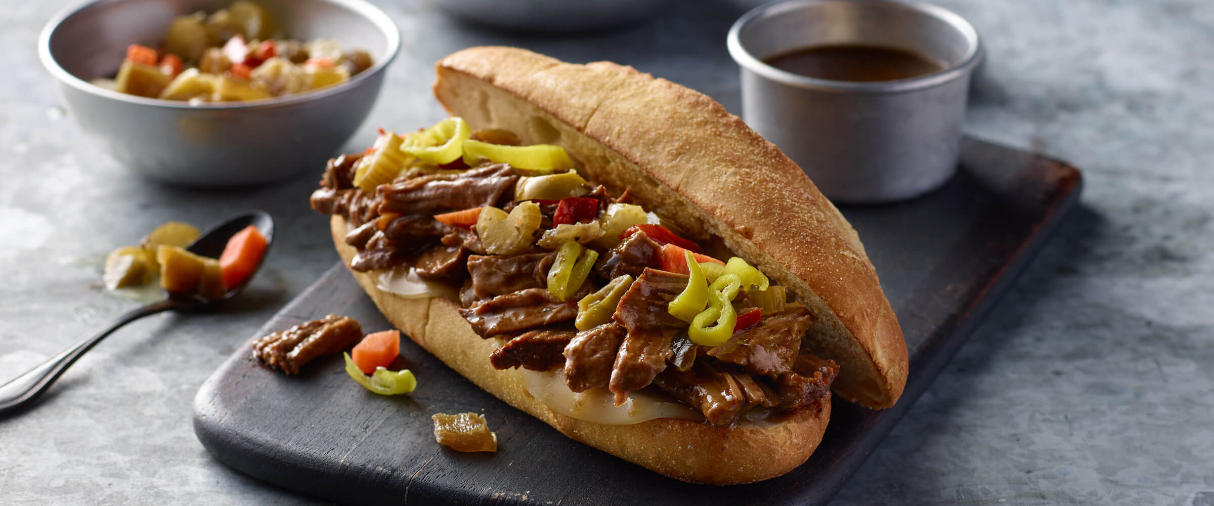 Italian Beef Sandwich on black platter with dipping sauce and extra topping