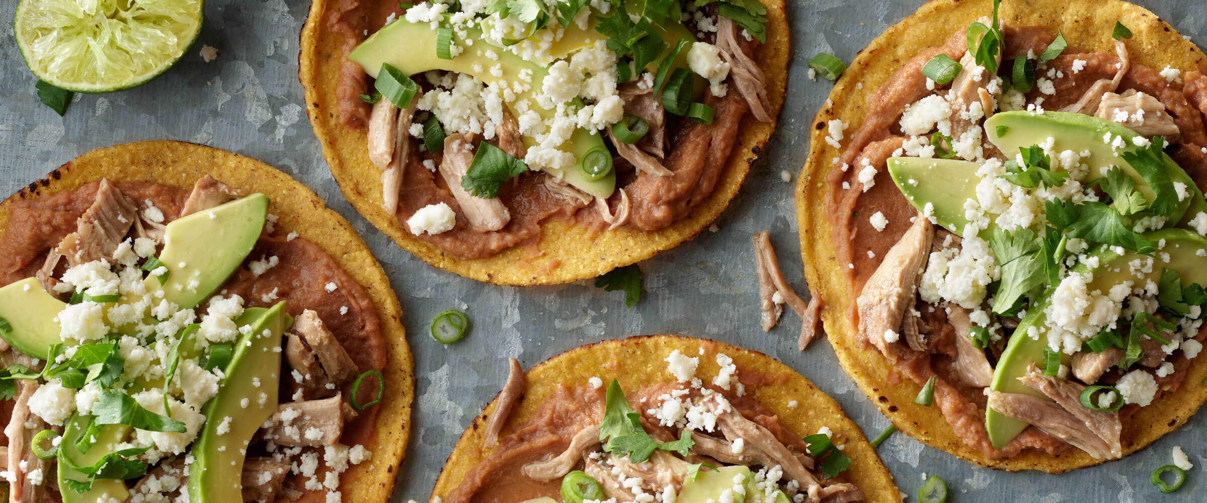 Pork Roast Tostadas topped with cheese, greens and avocado on gray platter