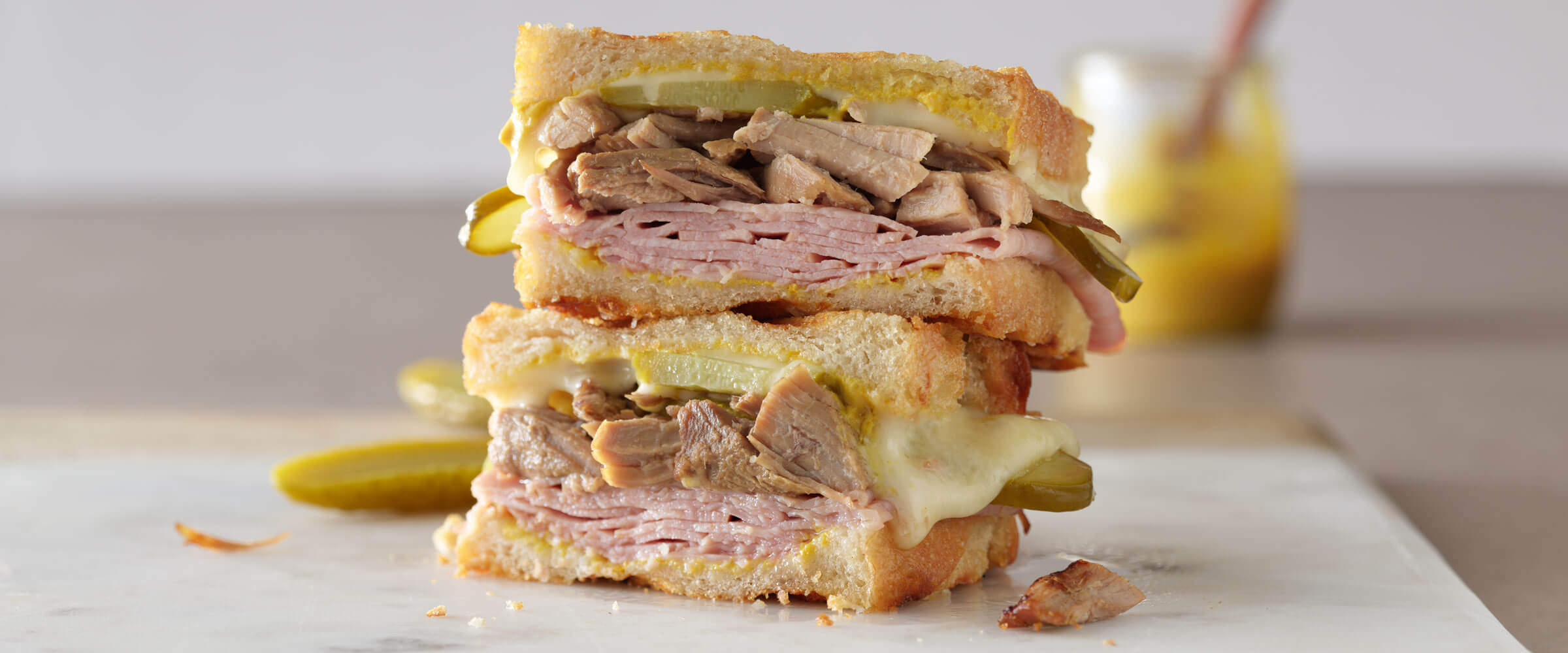 Pork Roast and Ham Cubano stacked high on white platter with pickles