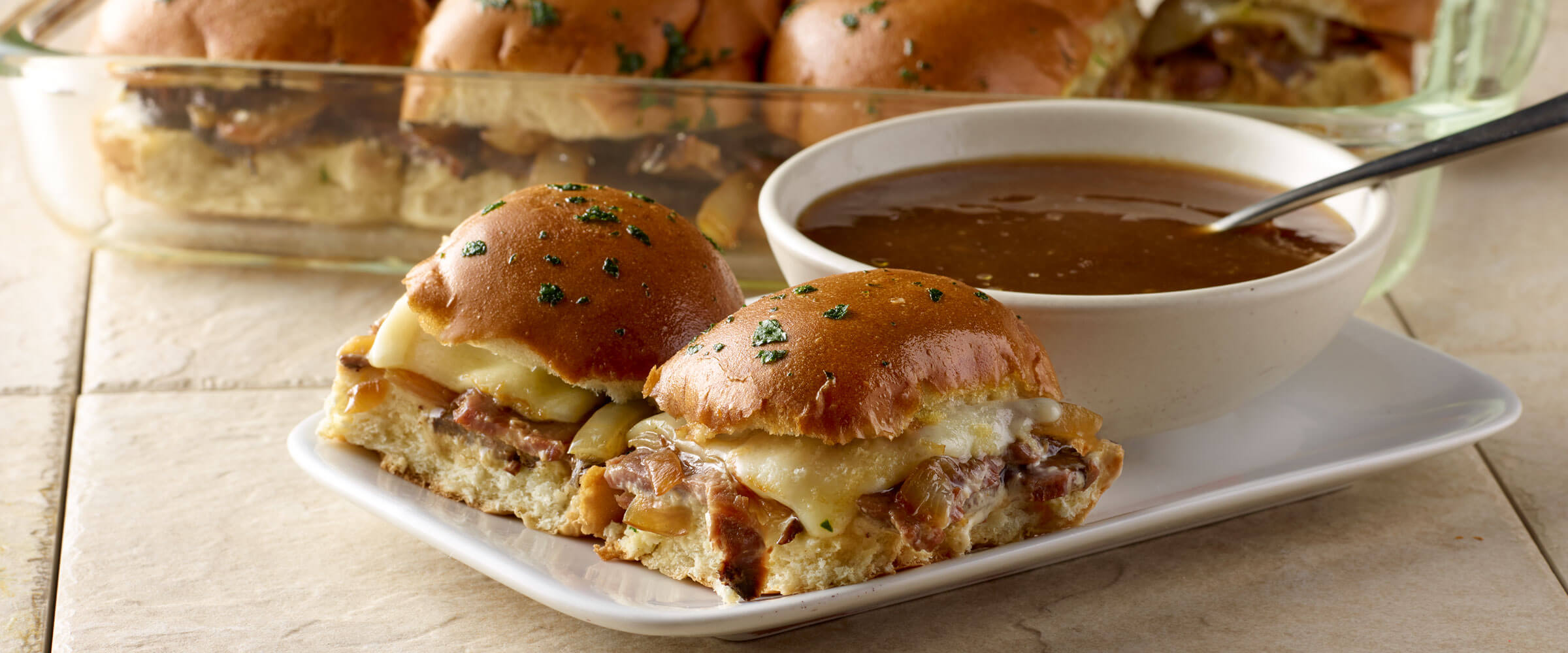 Roast Beef Sliders with Caramelized Onions on white plate with dipping sauce