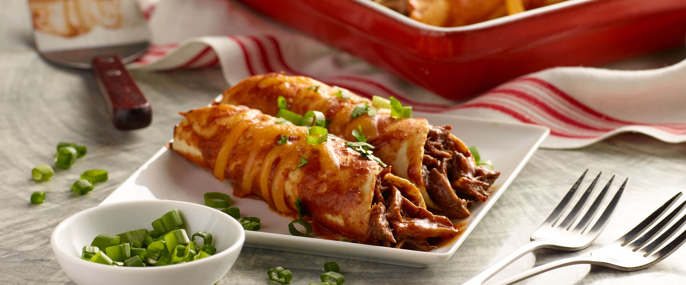 Shredded Beef Enchiladas on white plate with green onions to garnish