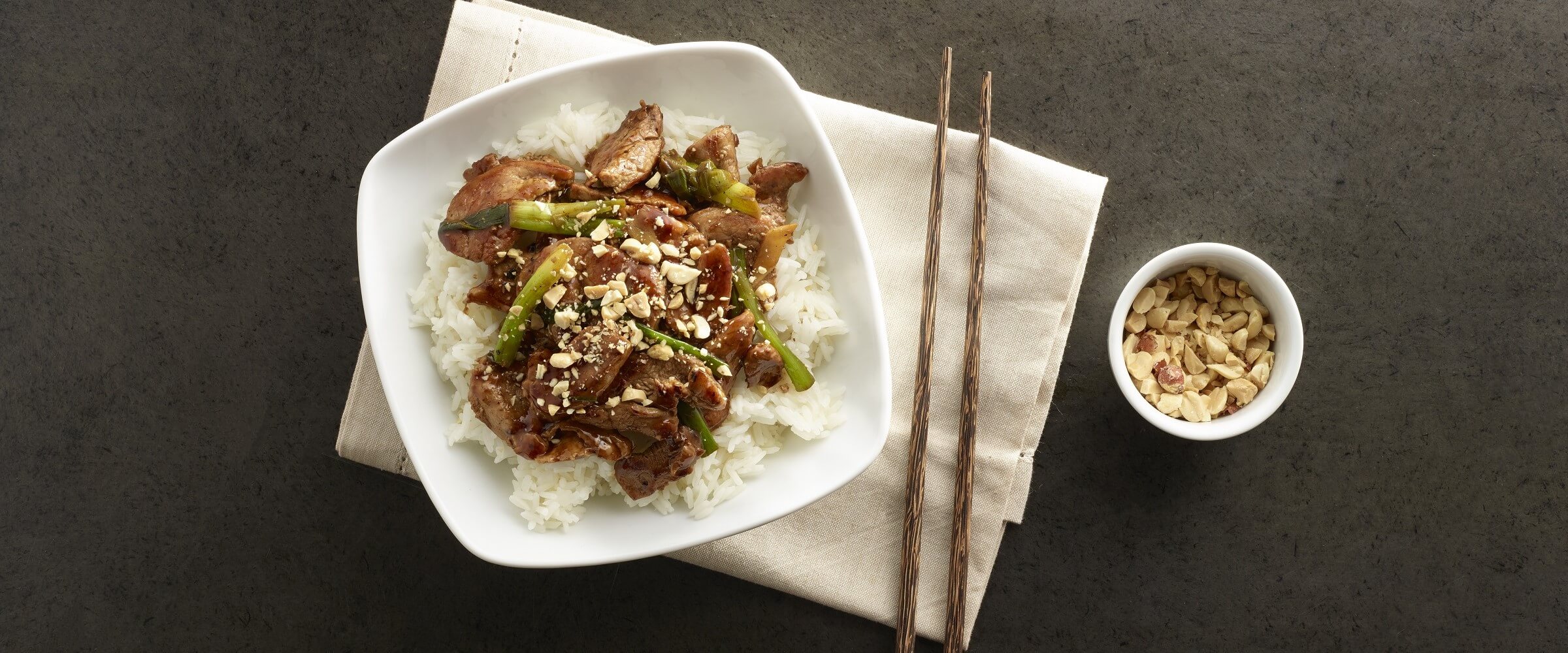 stir fry pork with peanut sauce over rice in white bowl with chopsticks