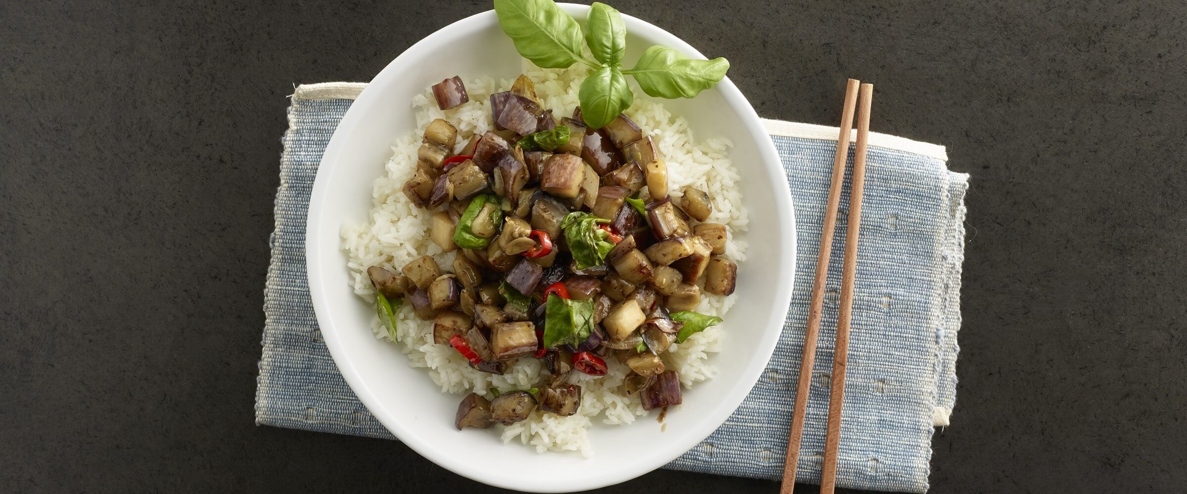 thai basil eggplant over rice in white bowl with chopsticks
