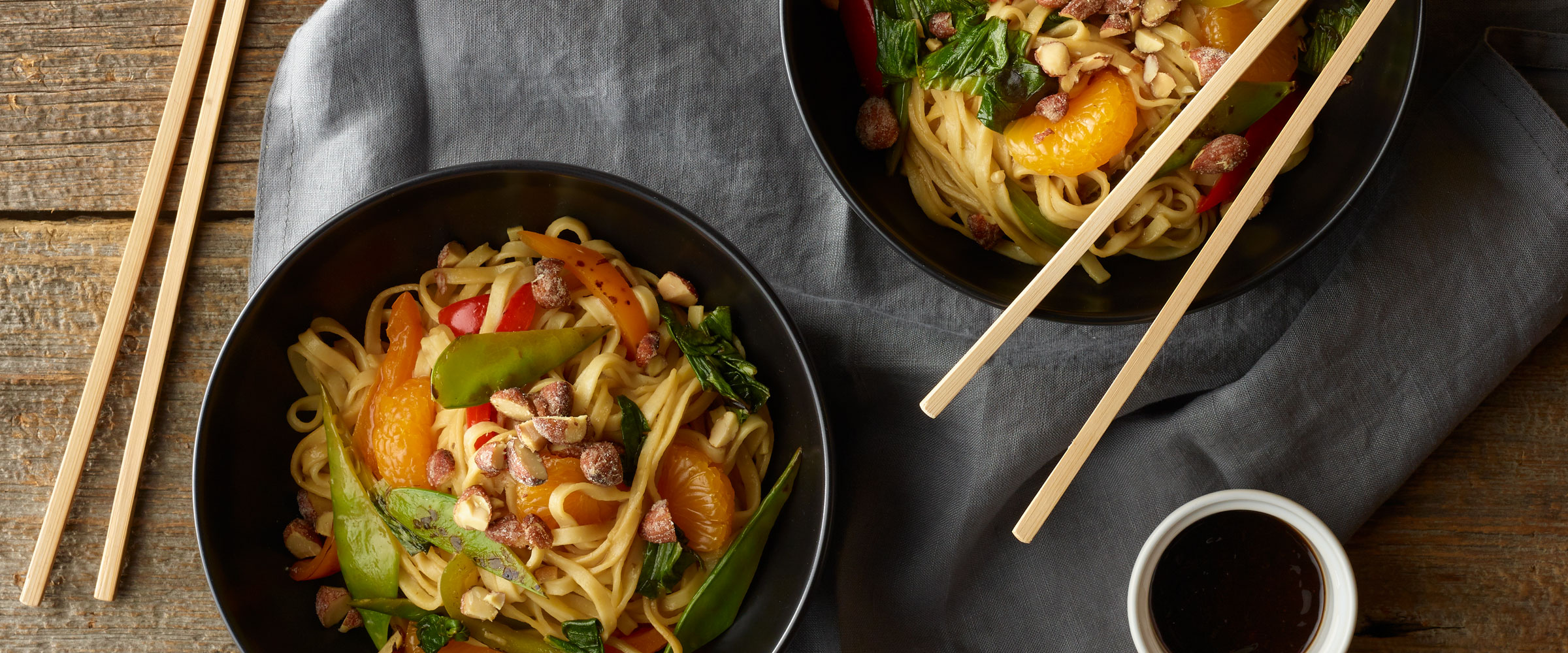 Citrus Chicken Lo Mein over noodles in black bowls with chopsticks