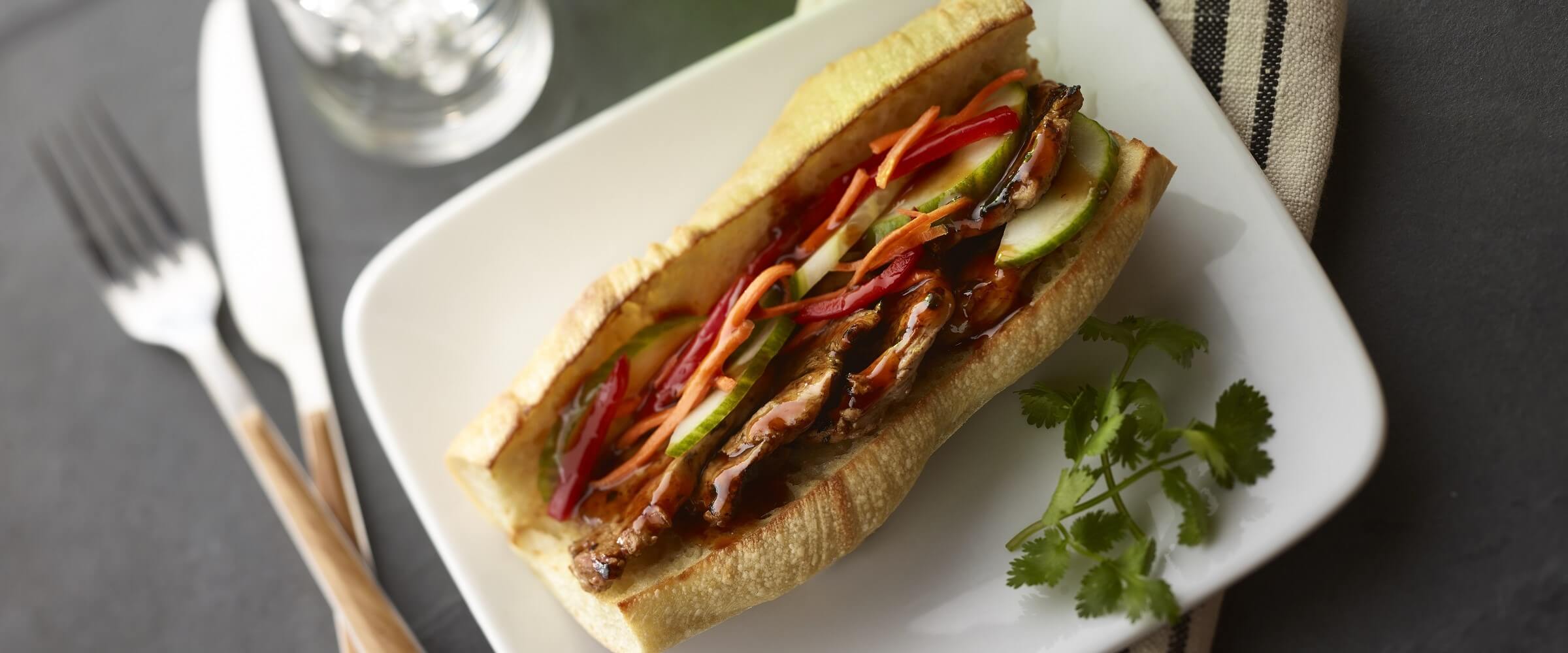 bahn mi sandwich with vegetables on white plate with garnish