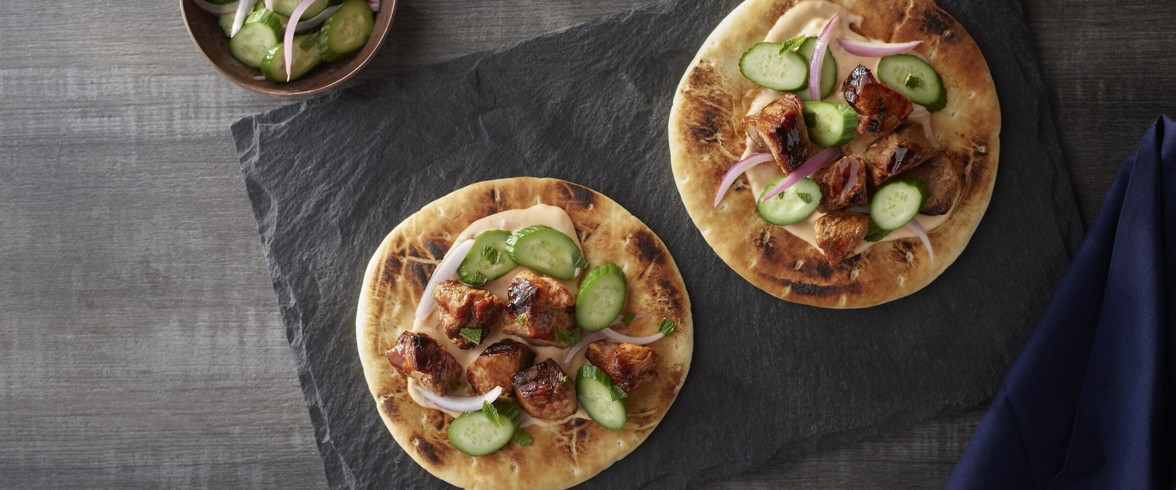 grilled pork pita skewers topped with cucumber and red onion on black board