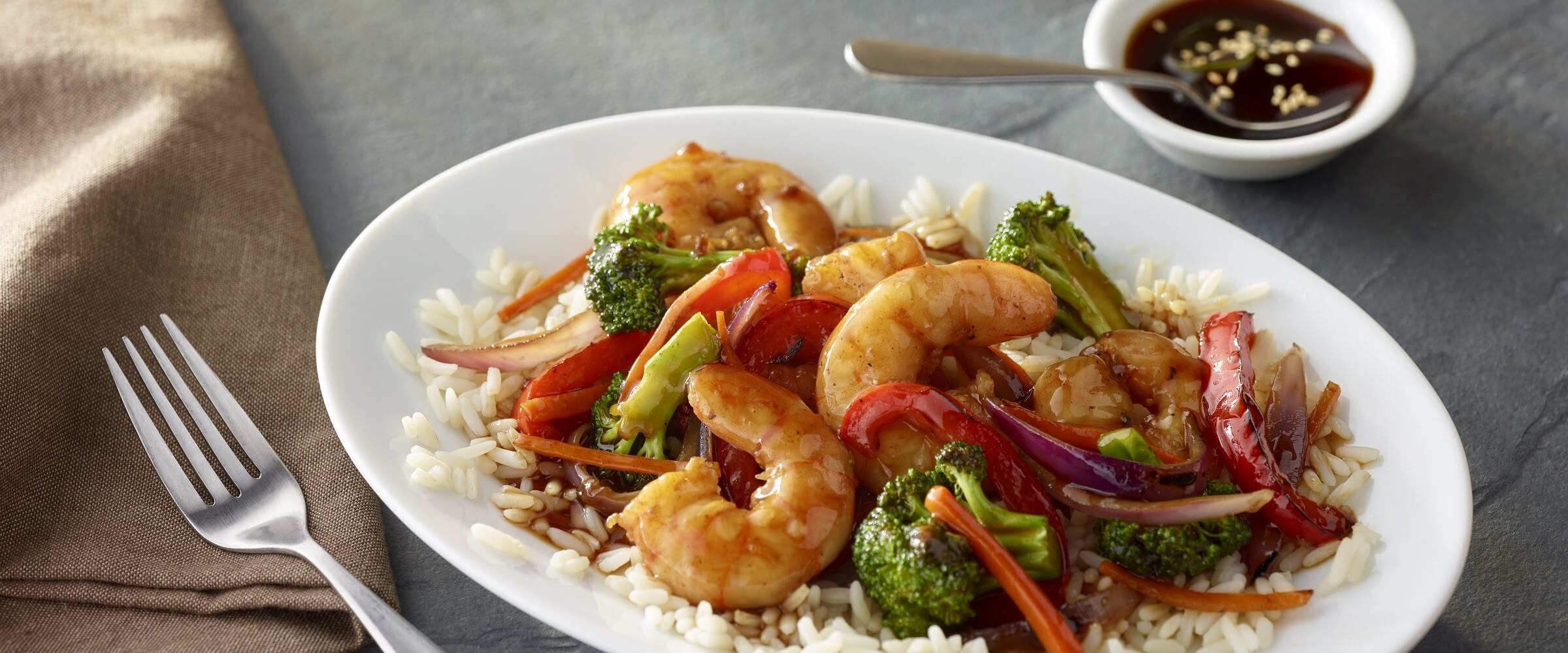 shrimp and broccoli stir fry over rice in white bowl with extra sauce on the side