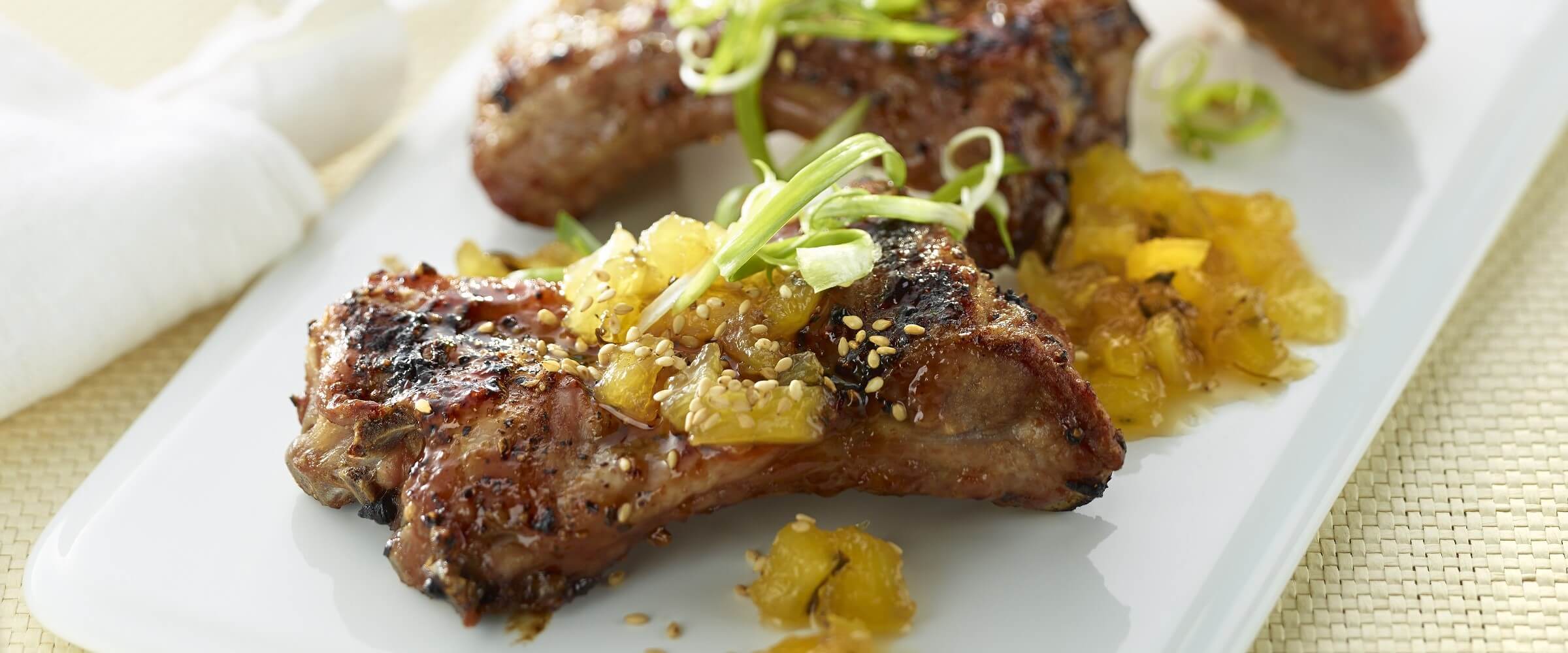 sticky pork ribs with pineapple chutney on white plate with green onions