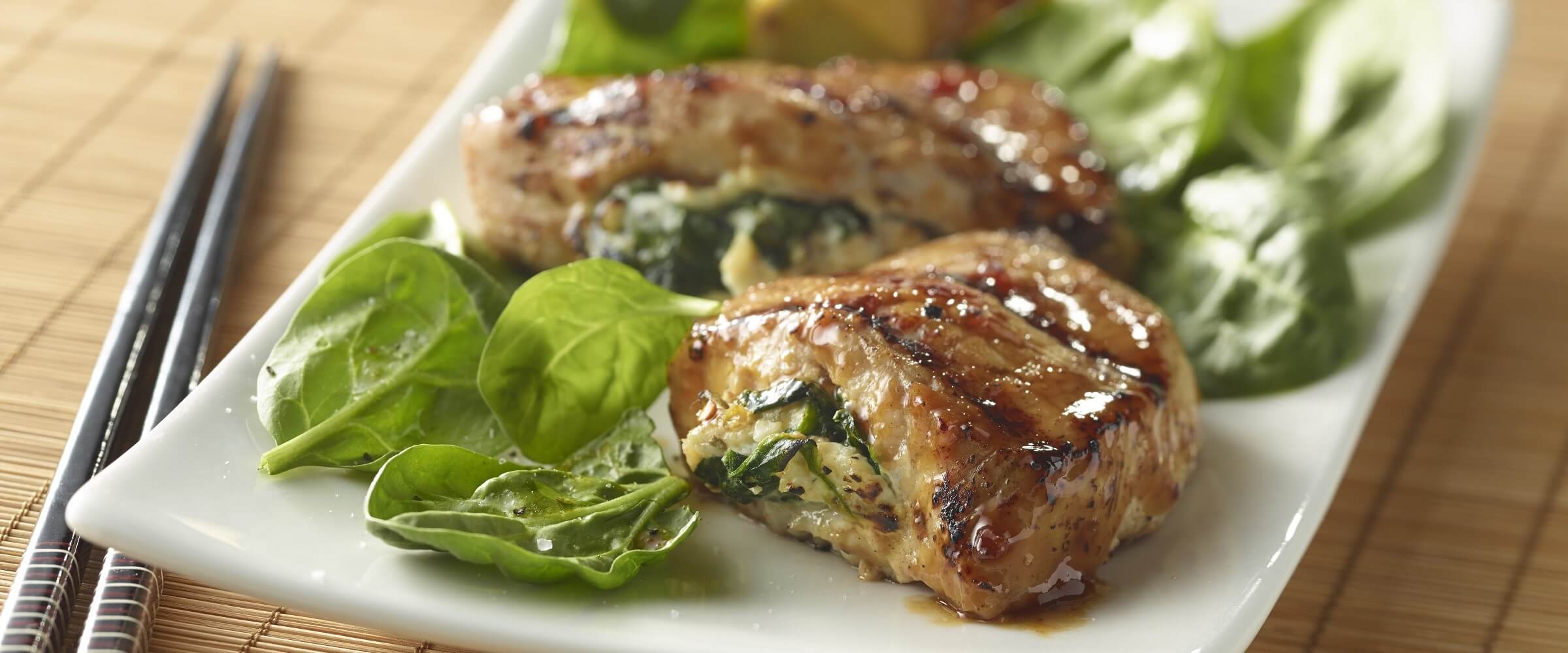stuffed spicy pork chops on white plate with spinach and chopsticks