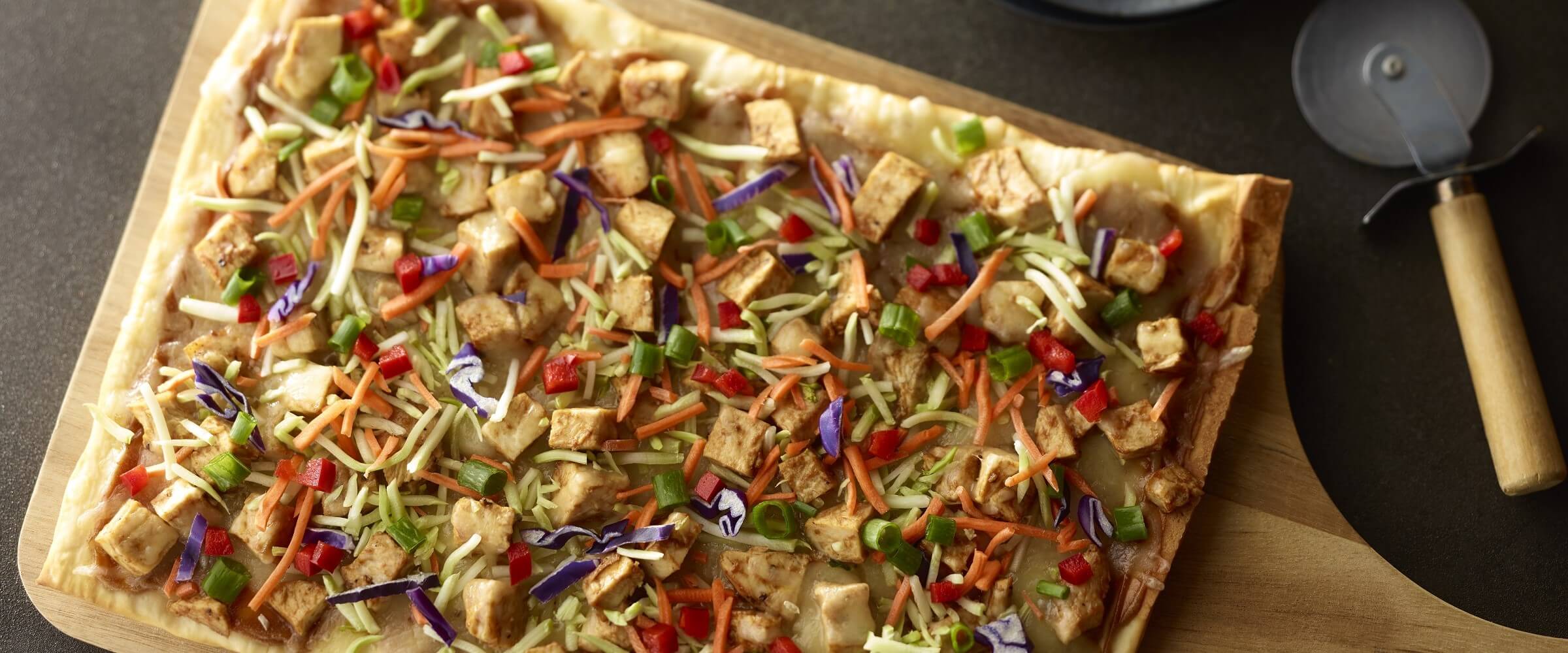thai chicken pizza on peel with pizza cutter