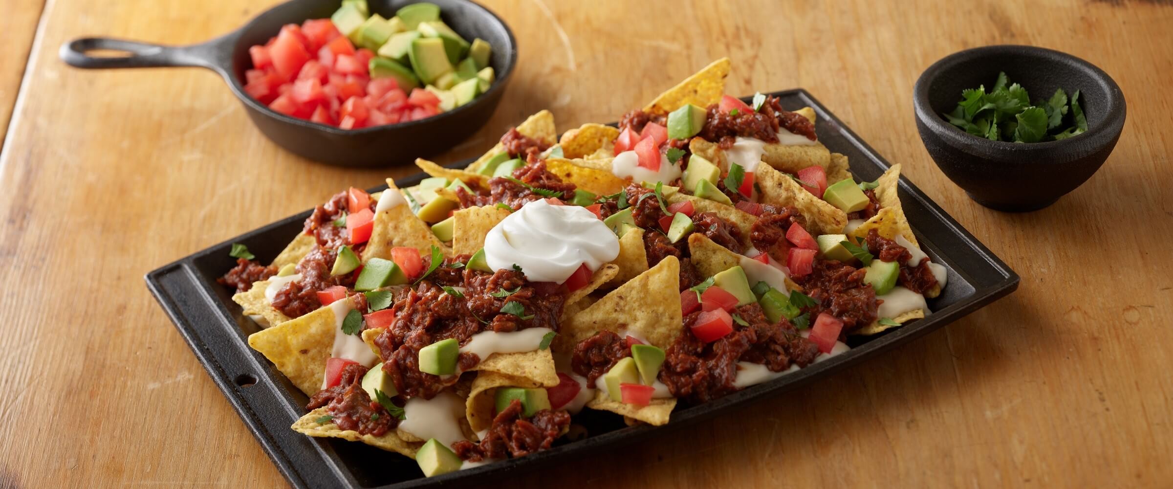 BBQ beef nachos on plate sheet pan topped with sour cream, tomatoes and avocado