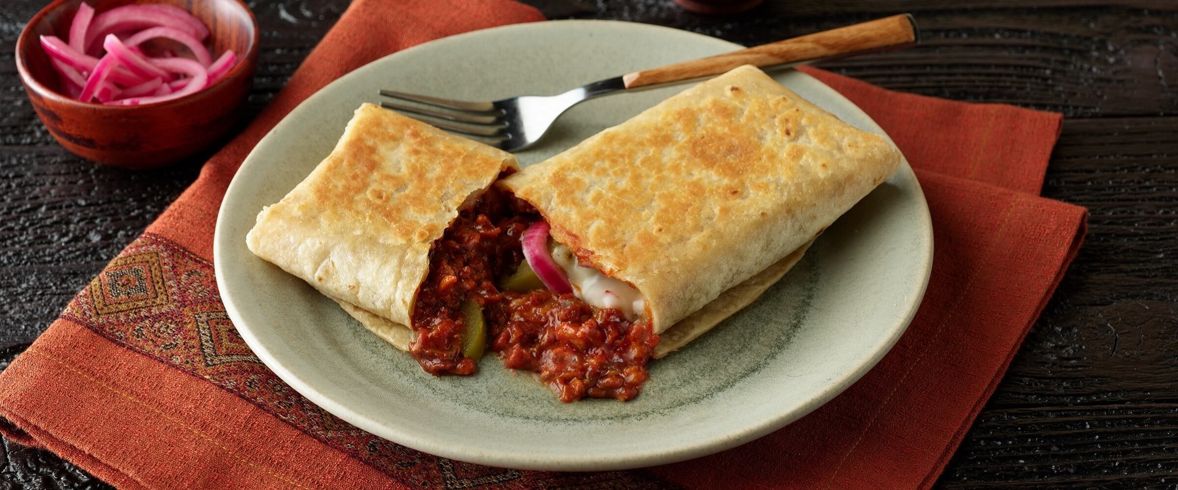 BBQ pork burrito on plate on orange napkin with side of red onions