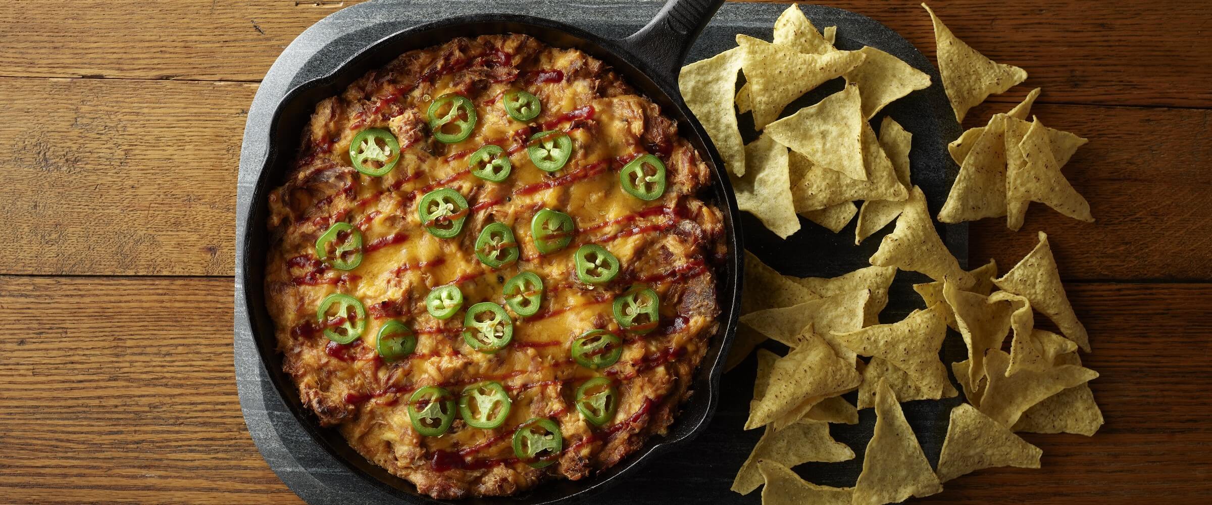 BBQ pulled pork dip topped with cheese and jalapenos in skilled with chips on the side