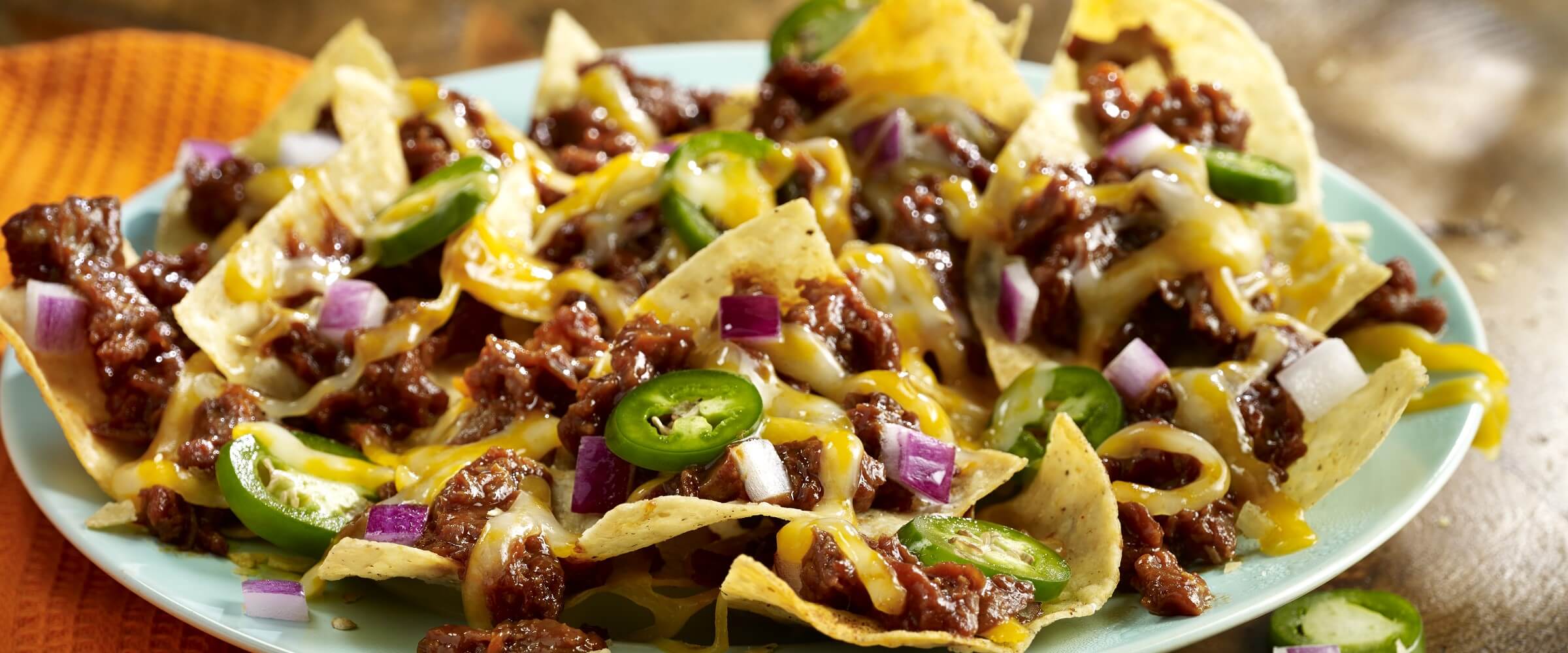 BBQ pork nachos on plate topped with cheese, red onion and jalapenos