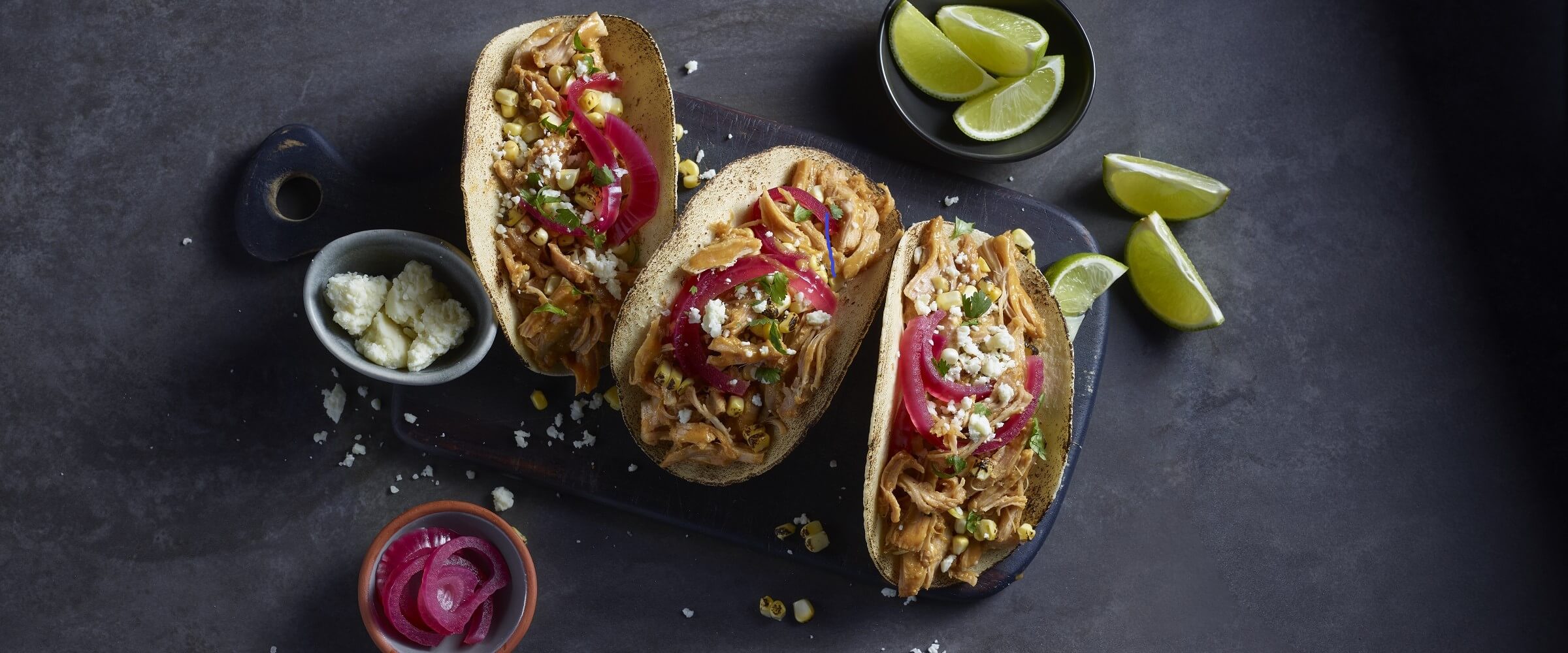 BBQ chicken street tacos topped with cheese and red onions on plate platter with side of lime wedges