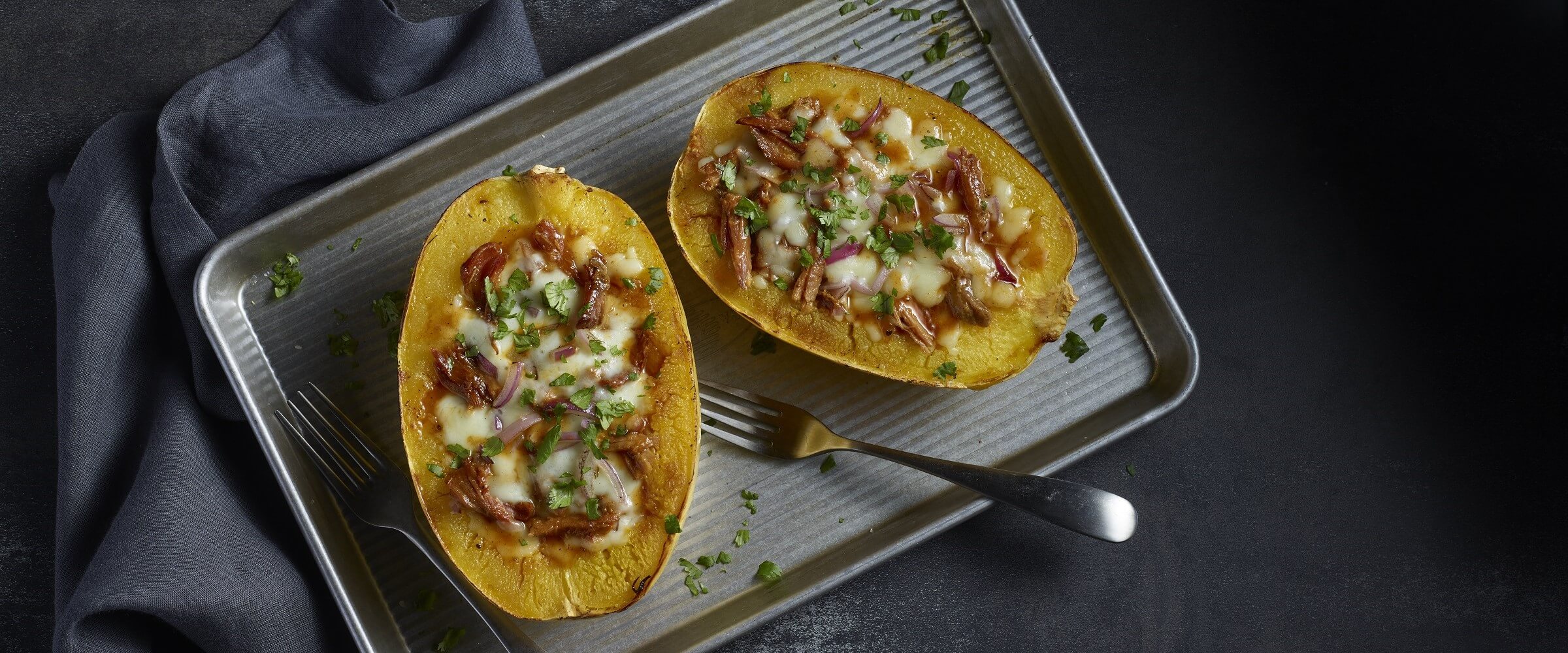 Pulled pork stuffed spaghetti squash topped with cheese on sheet pan with forks