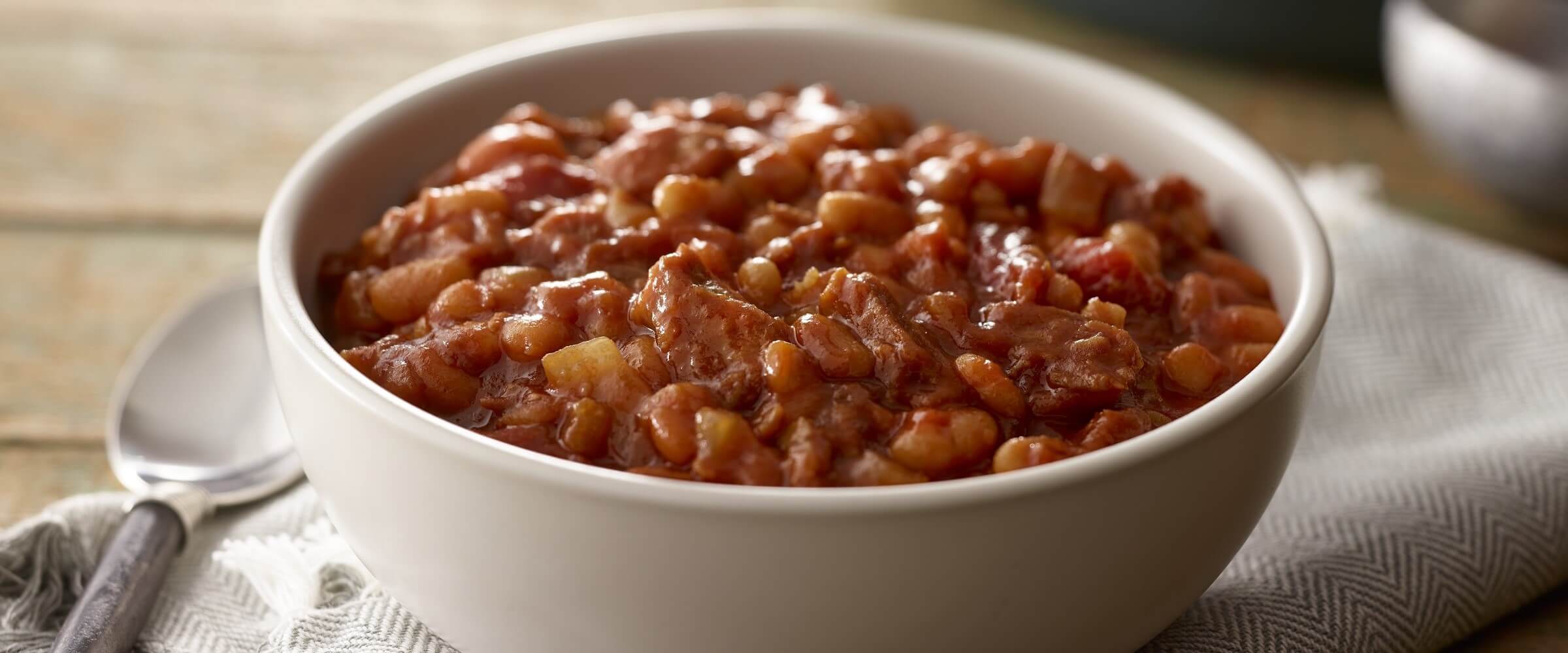 BBQ baked beans in bowl with spoon on cream napkin