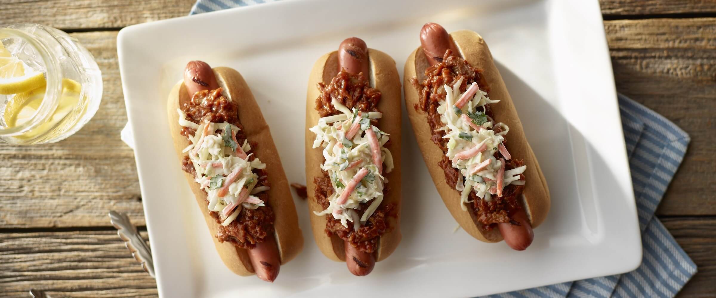 BBQ beef slaw dogs on white plate with striped napkin