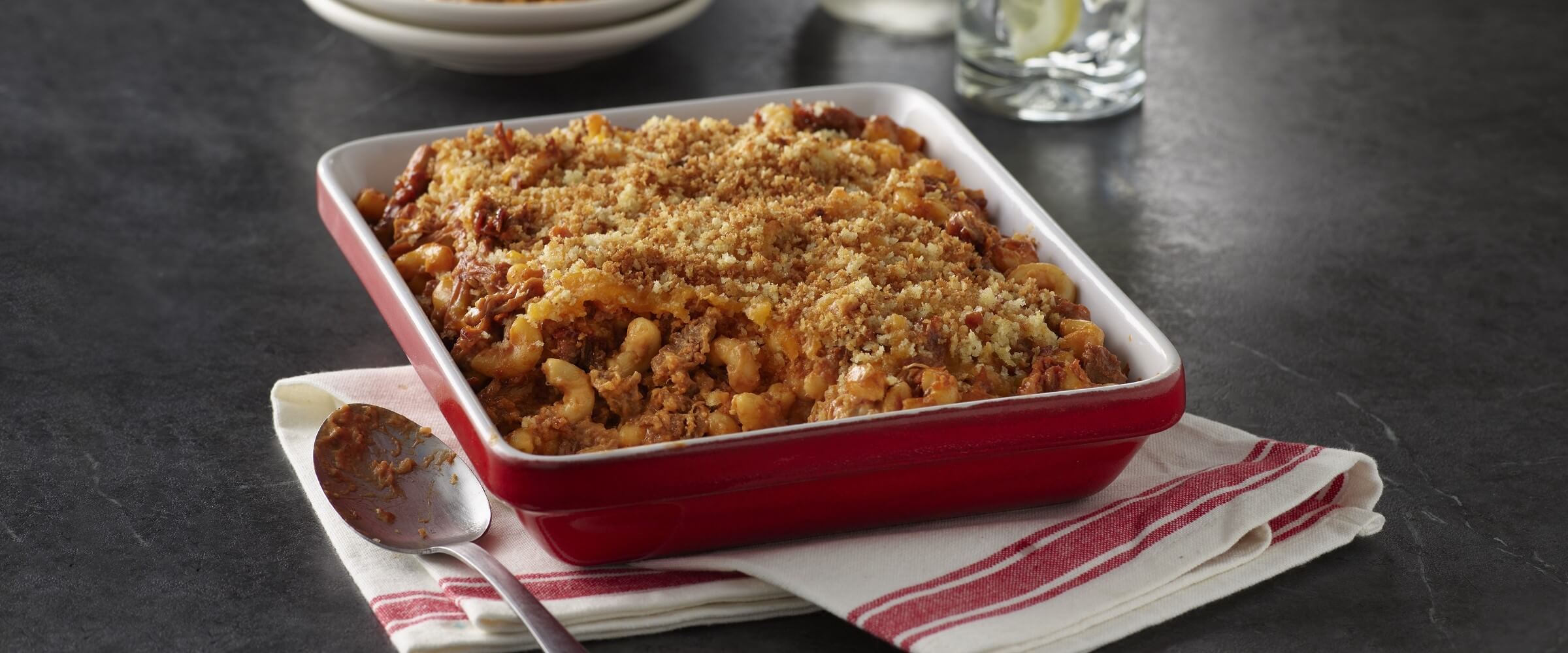 BBQ pulled pork macaroni and cheese topped with breadcrumbs in red dish on a striped napkin