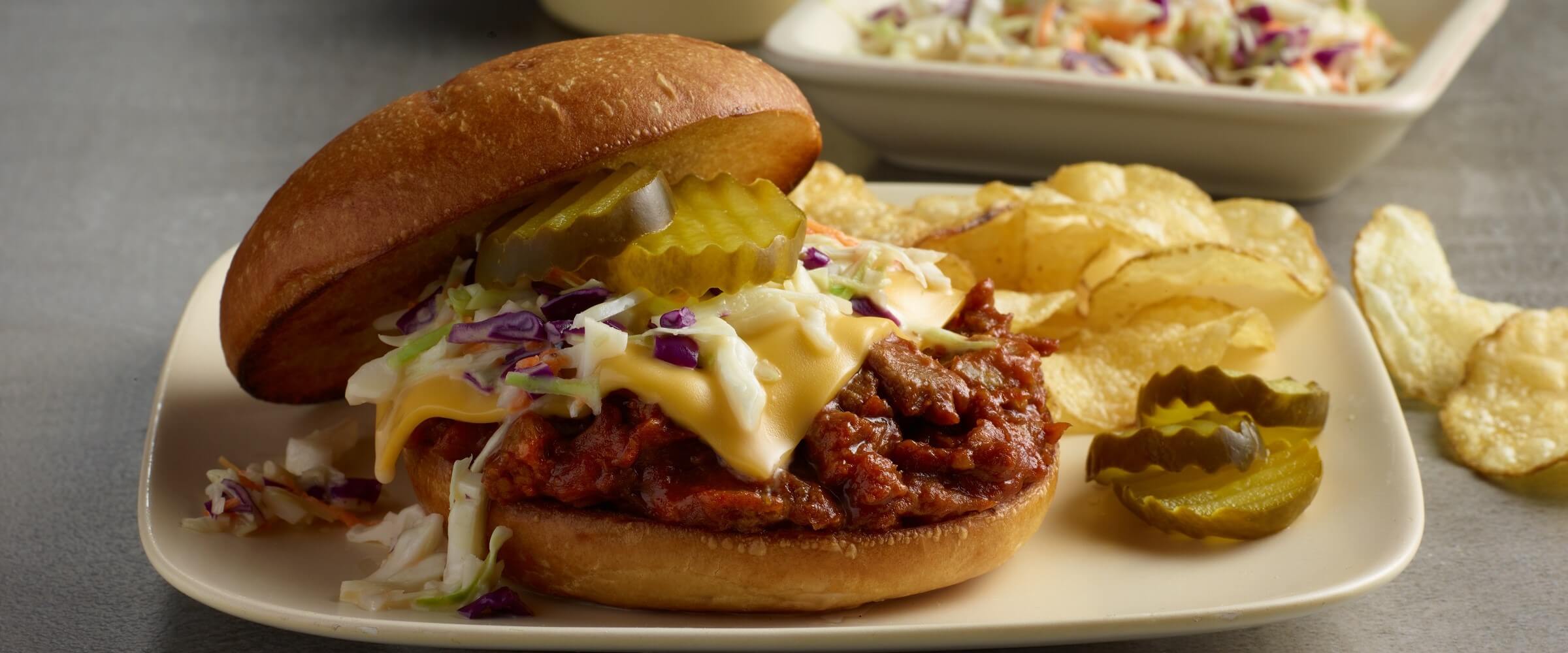 BBQ pork burgers topped with slaw, cheese and pickles with potato chips on plate