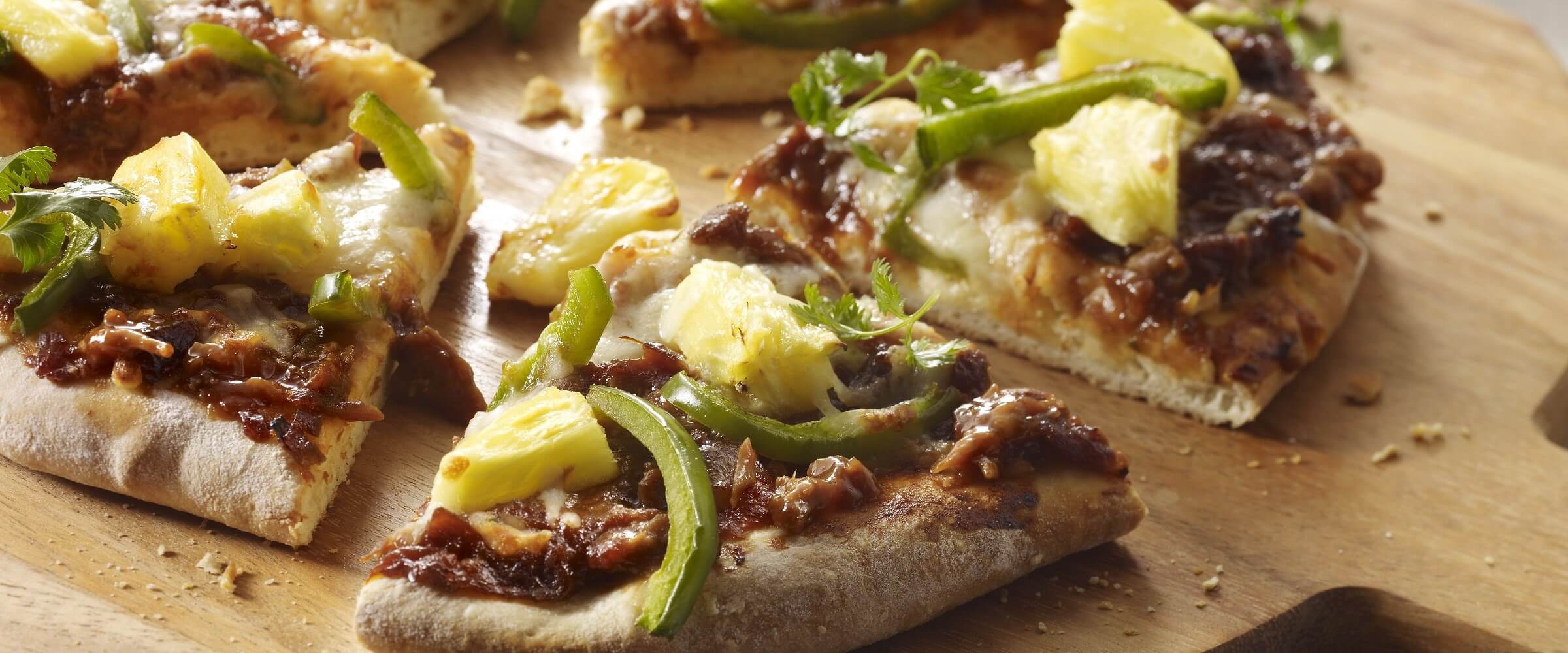Mini BBQ pizza topped with green peppers and pineapple on a wood pizza board