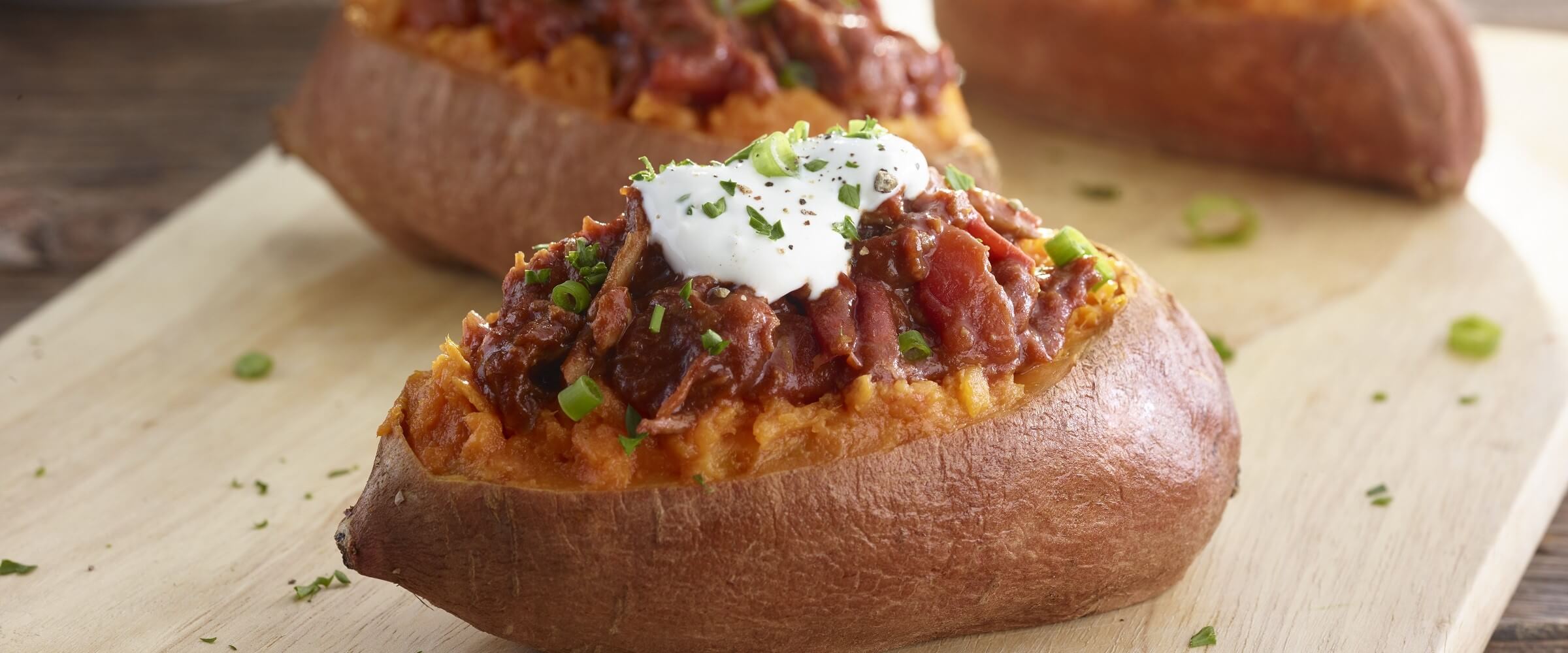 BBQ pulled pork stuffed sweet potato topped with sour cream on wood platter