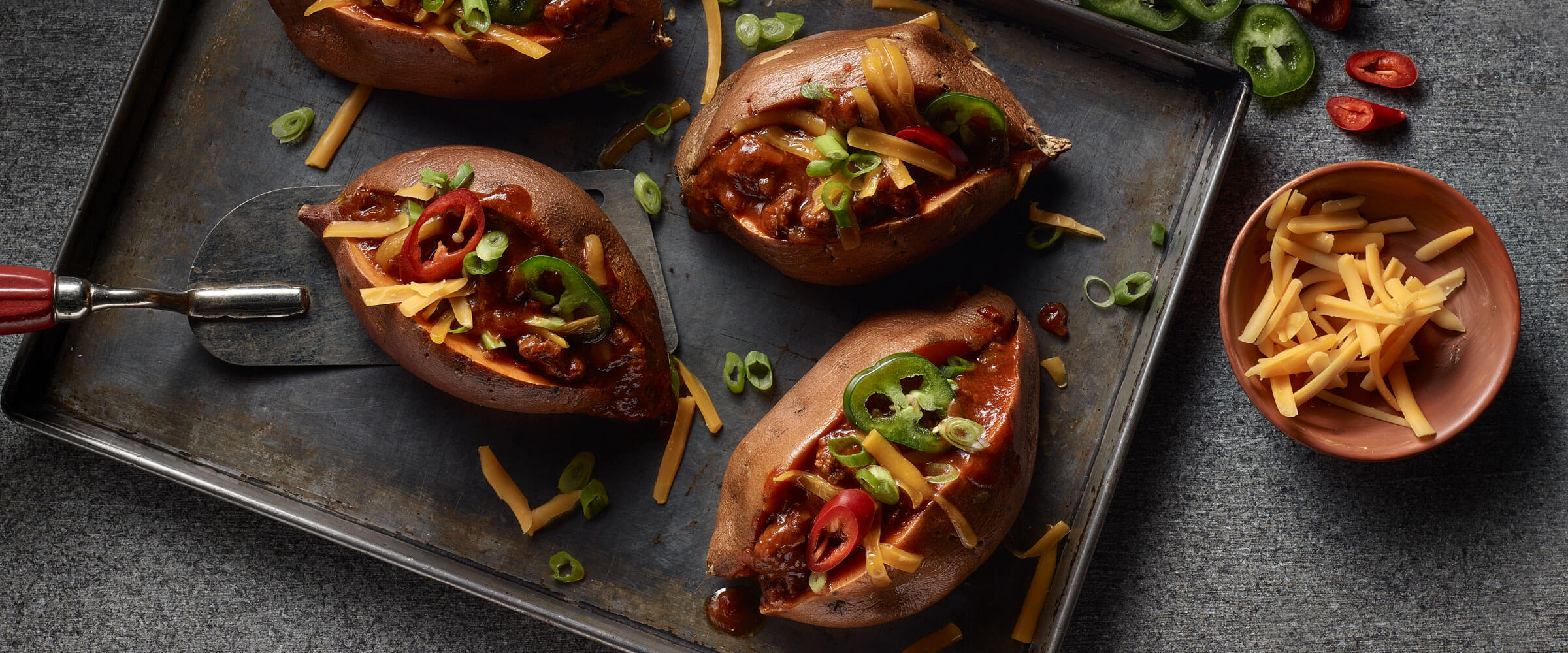Chili Stuffed Sweet Potatoes topped with cheese and jalapenos on sheet pan