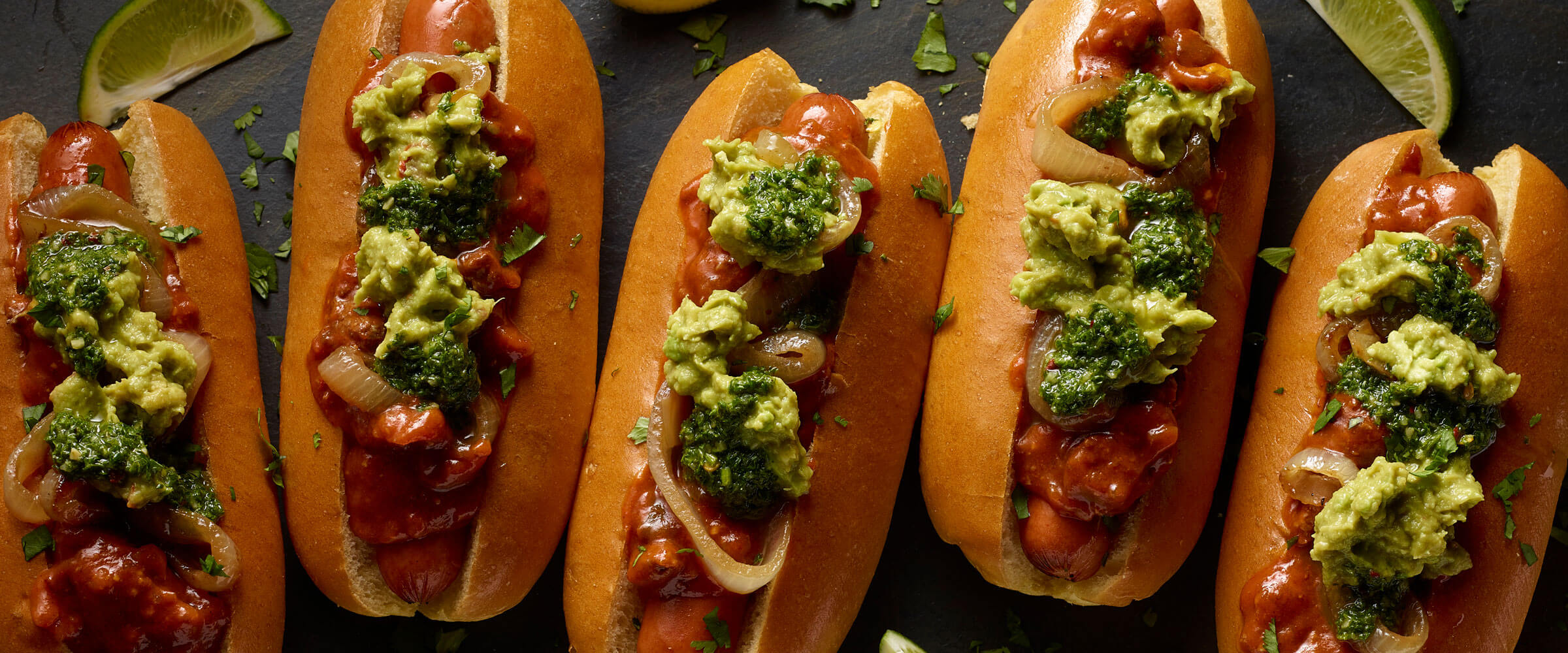 Chili Green Dogs topped with broccoli and guacamole with lime wedges