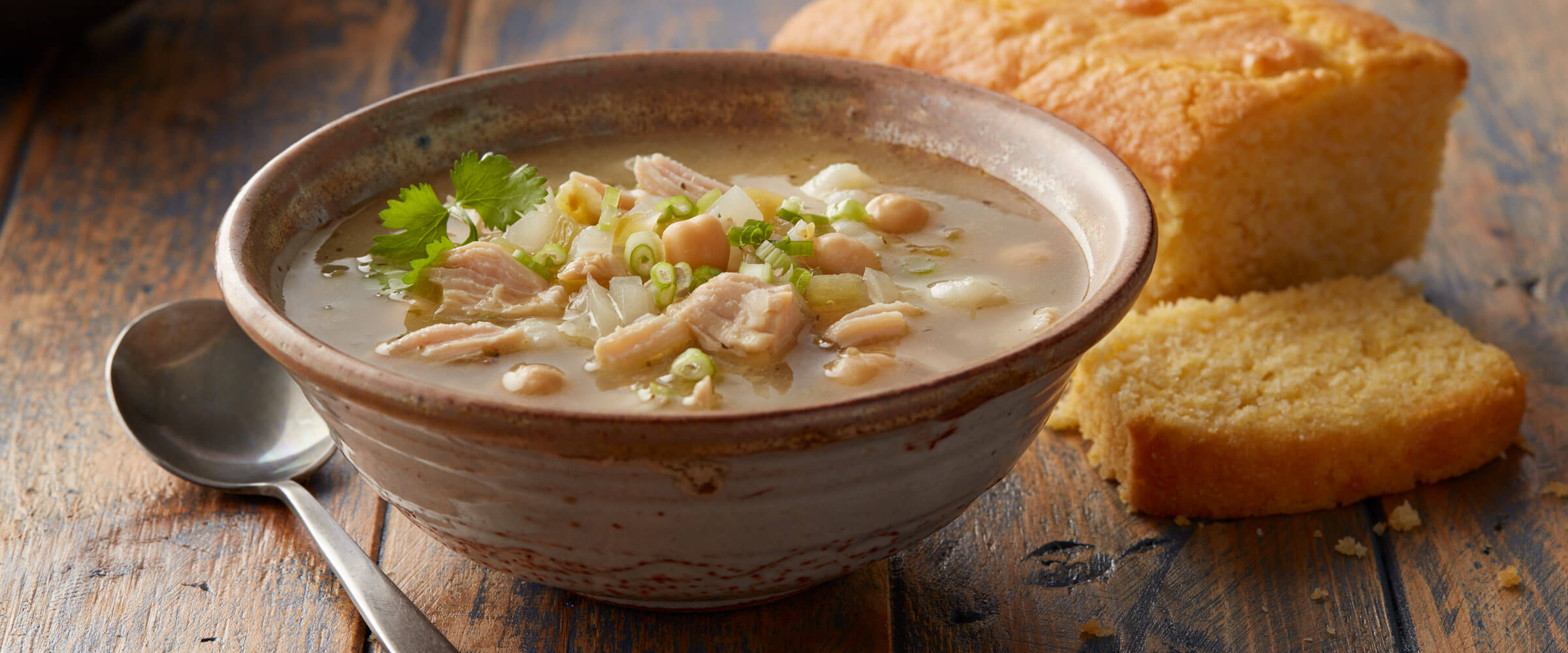 White Chicken Chili in brown bowl with loaf of corn bread