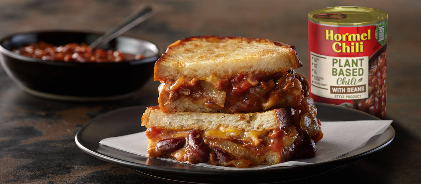 Plant-based chili can next to chili sandwich on black plate