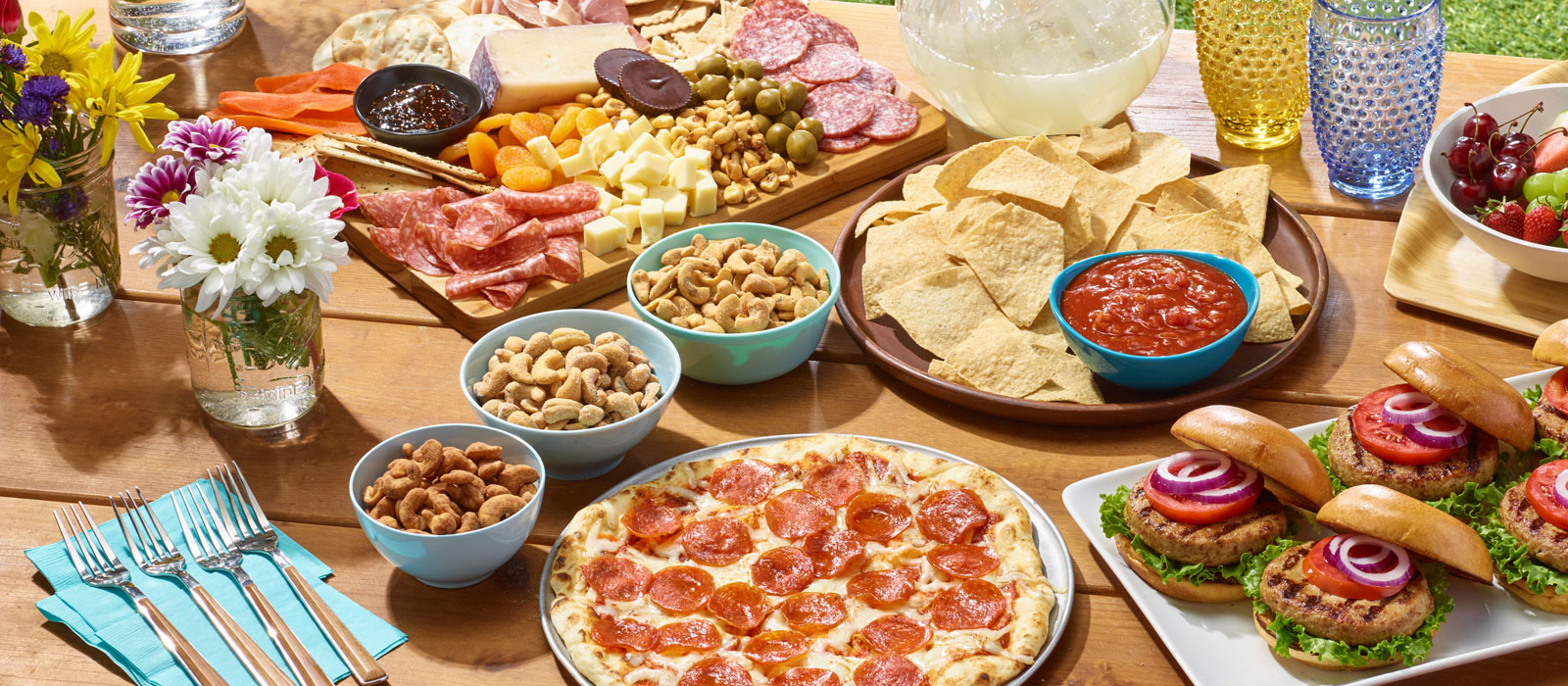 Summer themed picnic spread with pizza, snack nuts, charcuterie, burgers and snacks