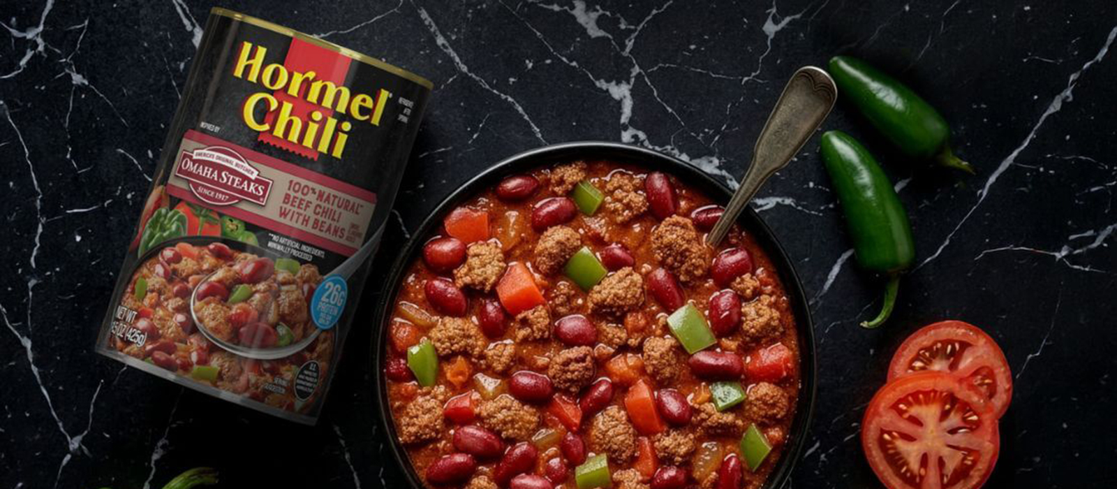 HORMEL® Chili & OMAHA STEAKS® 100% Natural Beef Chili with Beans can next to bowl full of HORMEL® Chili & OMAHA STEAKS® 100% Natural Beef Chili with Beans. A peppers, onion, and tomatoes surround the product.