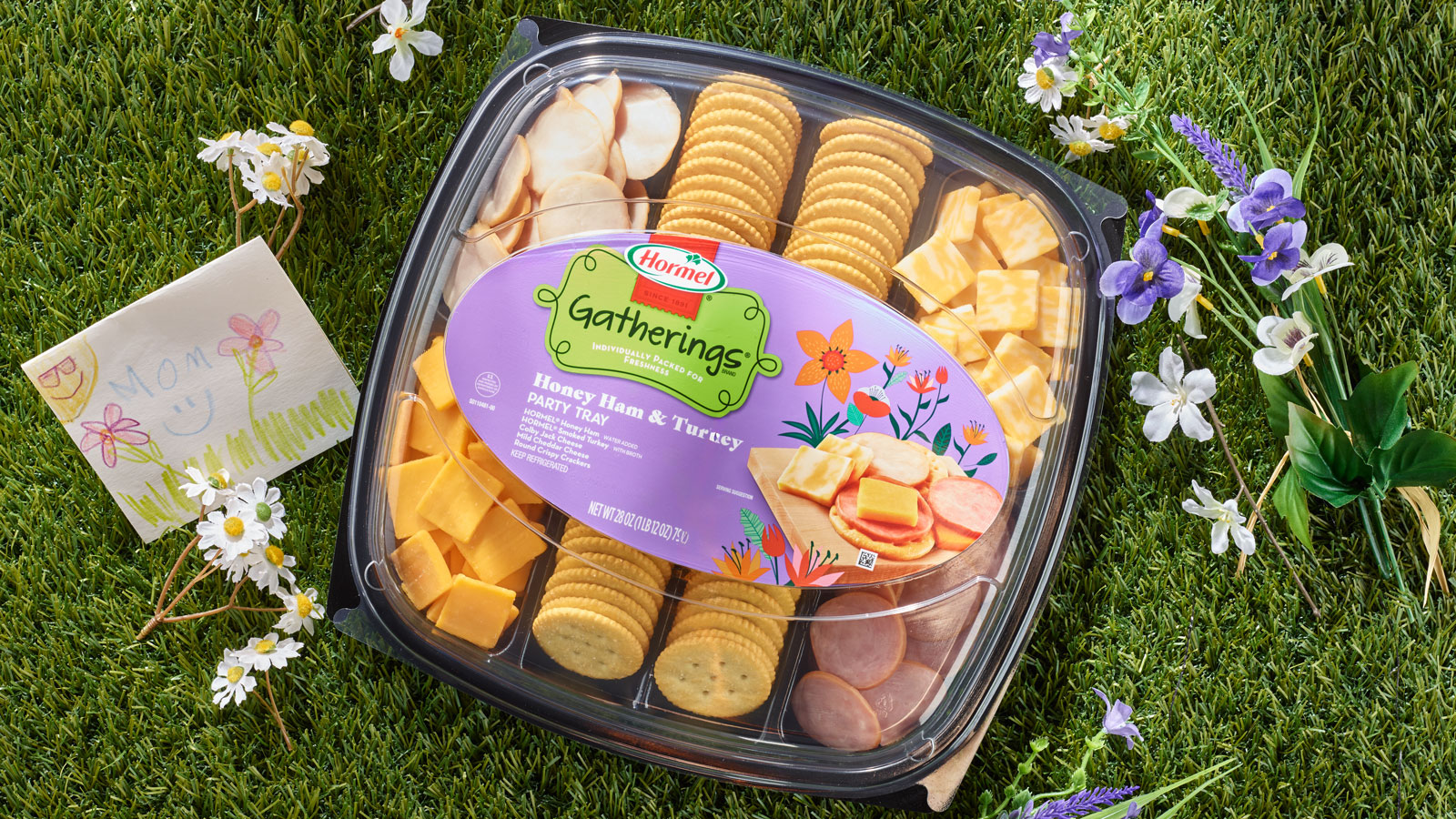 A honey ham and turkey party tray on a bed of grass with flowers