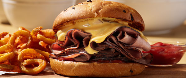 roast beef sandwich on a bun with melting cheese and a side of crispy curly fries and ketchup