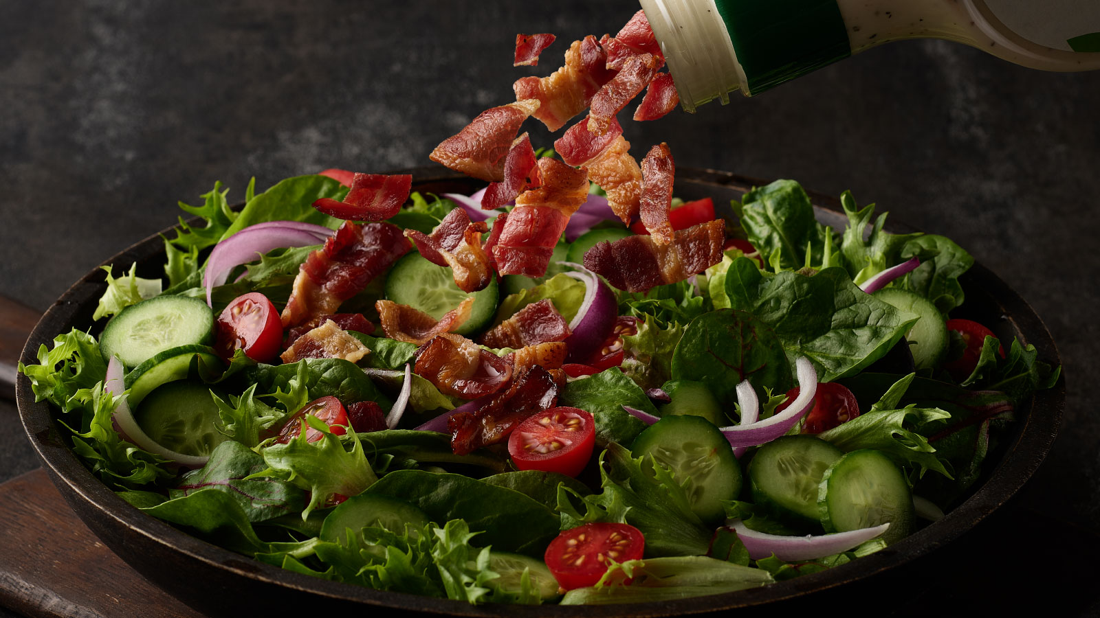 Ranch bacon pouring out of a ranch bottle onto a salad